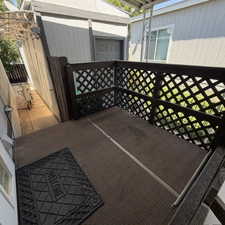 Outdoor patio space featuring a brown lattice railing and a brown textured floor. At the end of the driveway.