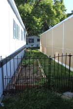 Private side yard featuring a black wrought-iron fence with a hinged gate, an enclosed garden bed, and mature trees providing natural shade