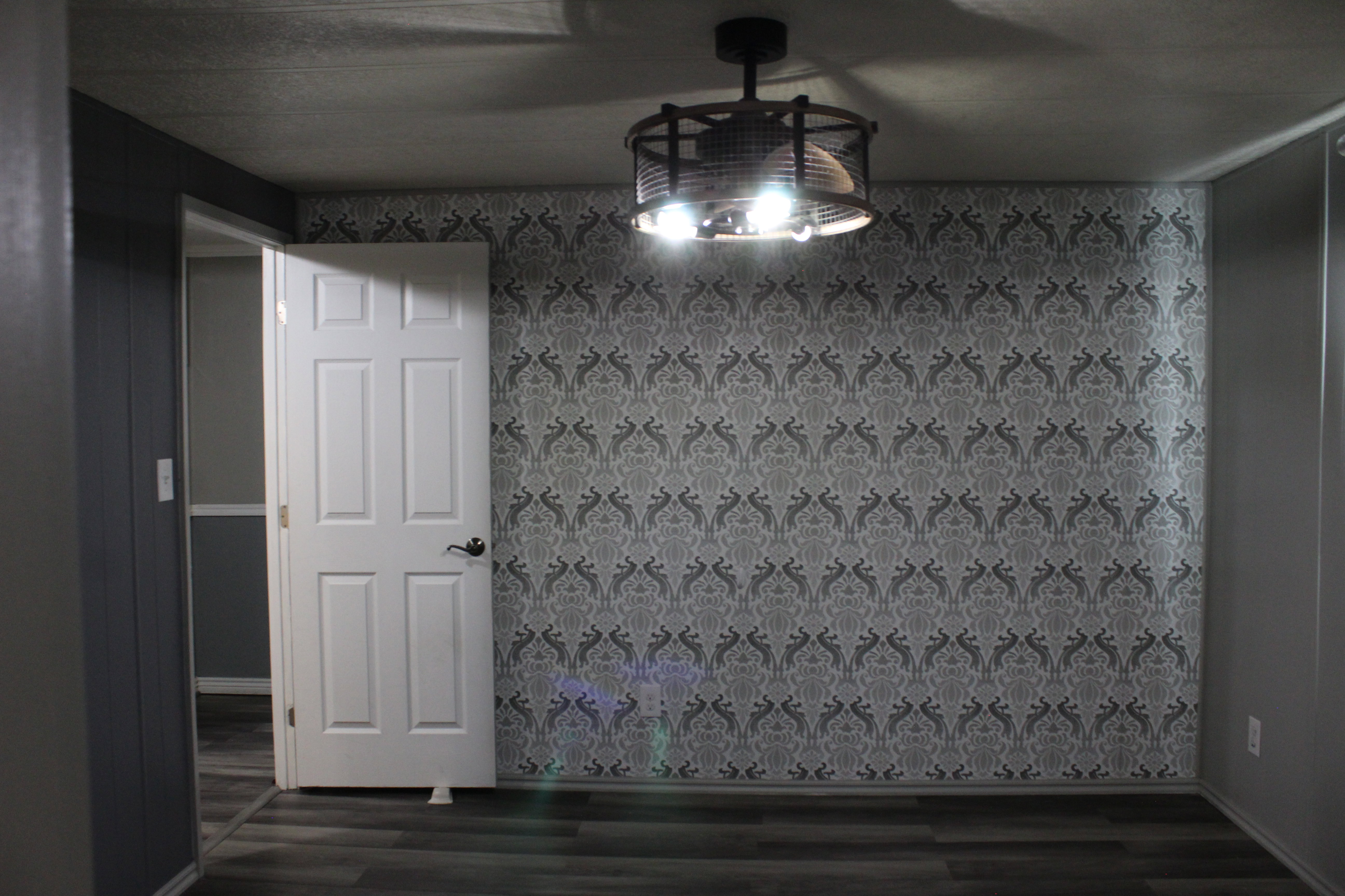 Primary Bedroom with Accent wall featuring grey patterned wallpaper, complemented by grey wood-finish flooring