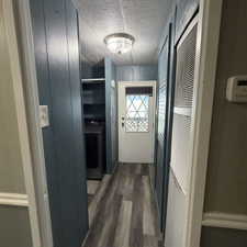 Hallway featuring wood-finish flooring, a flush-mount ceiling light fixture, a white door with decorative glass inserts, and a built-in shelving unit, a storm door, extra area for storage or cabinet along with washer and dryer.