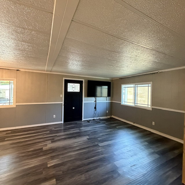 Spacious interior featuring wood-finish flooring, two-tone wall paneling, and multiple windows with horizontal grilles. view from the hallway entrance.