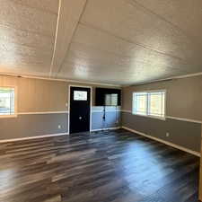 Spacious interior featuring wood-finish flooring, two-tone wall paneling, and multiple windows with horizontal grilles. view from the hallway entrance.