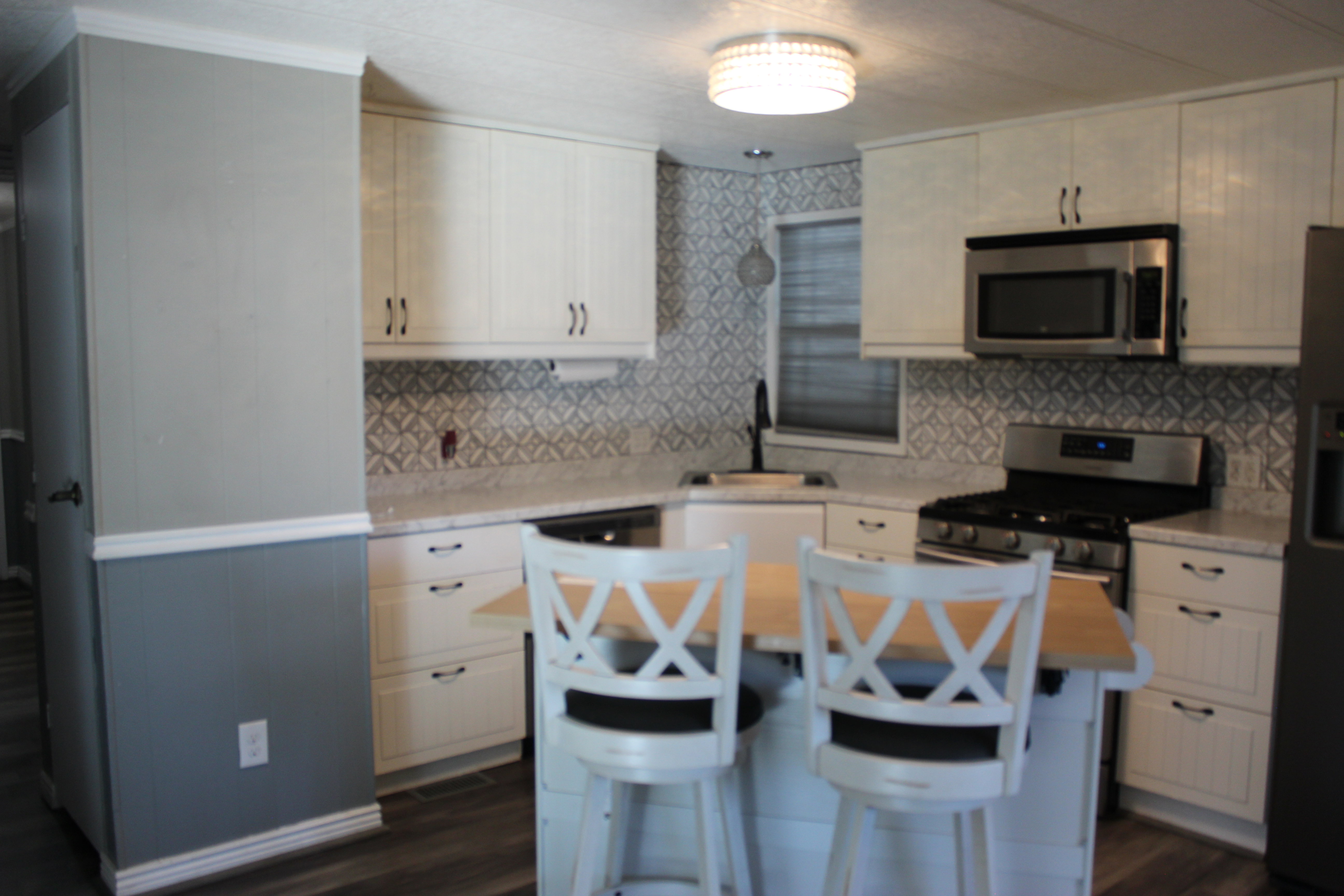 Kitchen featuring white cabinetry, light countertops, a patterned tile backsplash, stainless steel appliances, and wood-finish flooring