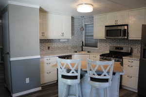 Kitchen featuring white cabinetry, light countertops, a patterned tile backsplash, stainless steel appliances, and wood-finish flooring