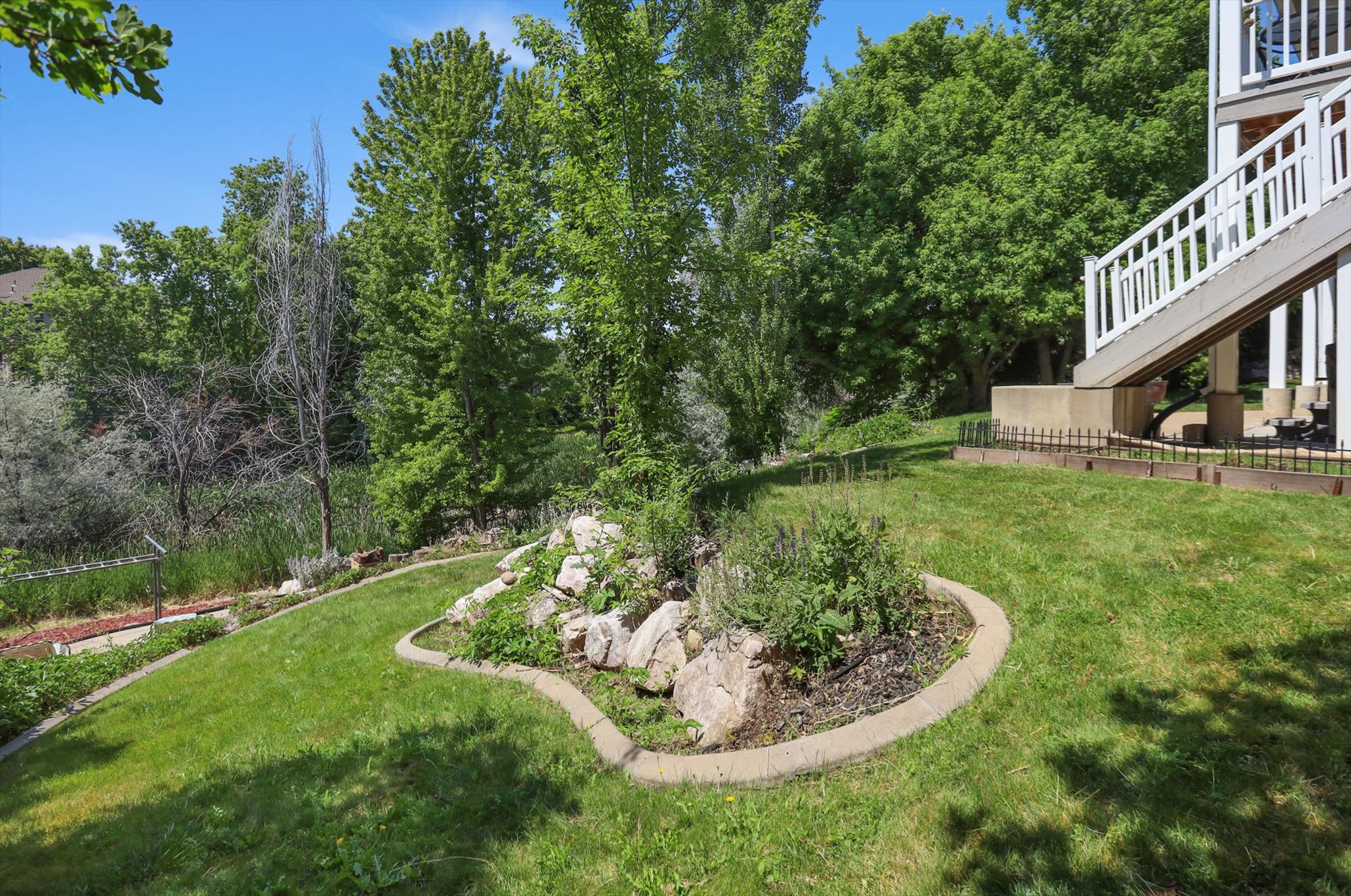 Manicured backyard featuring a concrete-edged rock garden, lush green lawn, and mature trees providing natural privacy