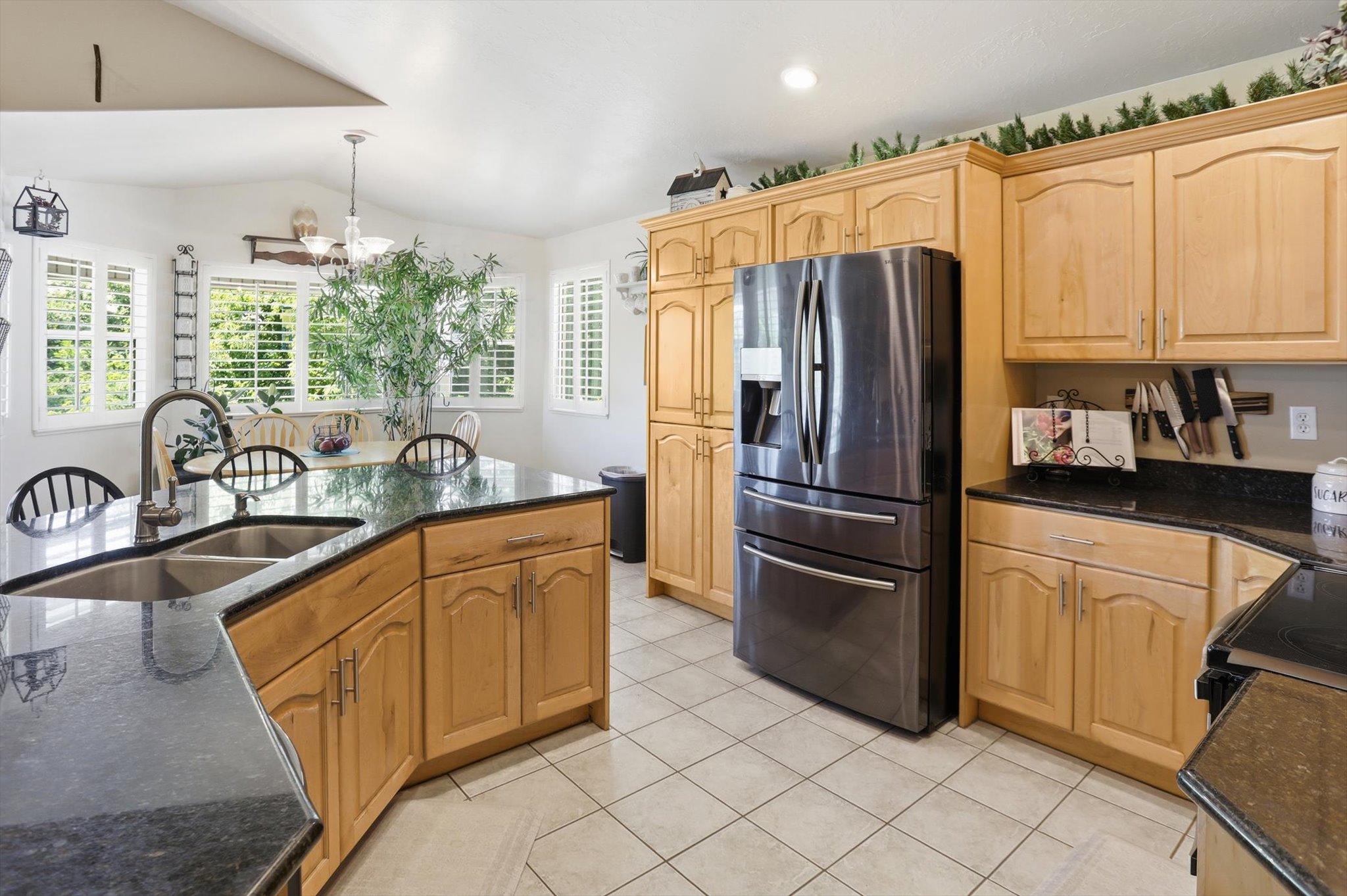 Kitchen featuring a double basin sink, dark stone countertops, wood cabinetry, stainless steel refrigerator, and tiled flooring