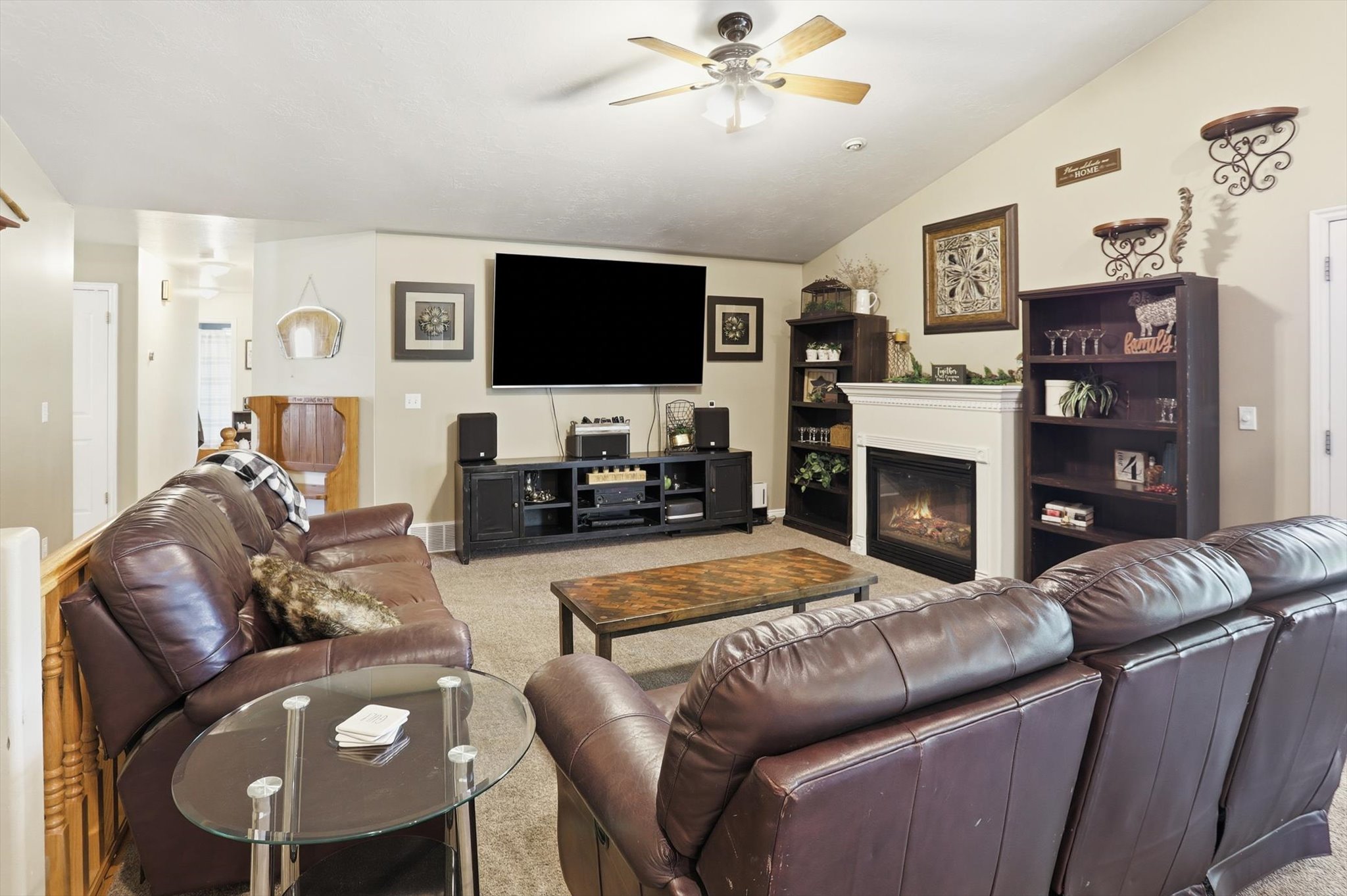 Vaulted ceiling living area featuring a ceiling fan with light, a fireplace with a white mantel, and built-in shelving