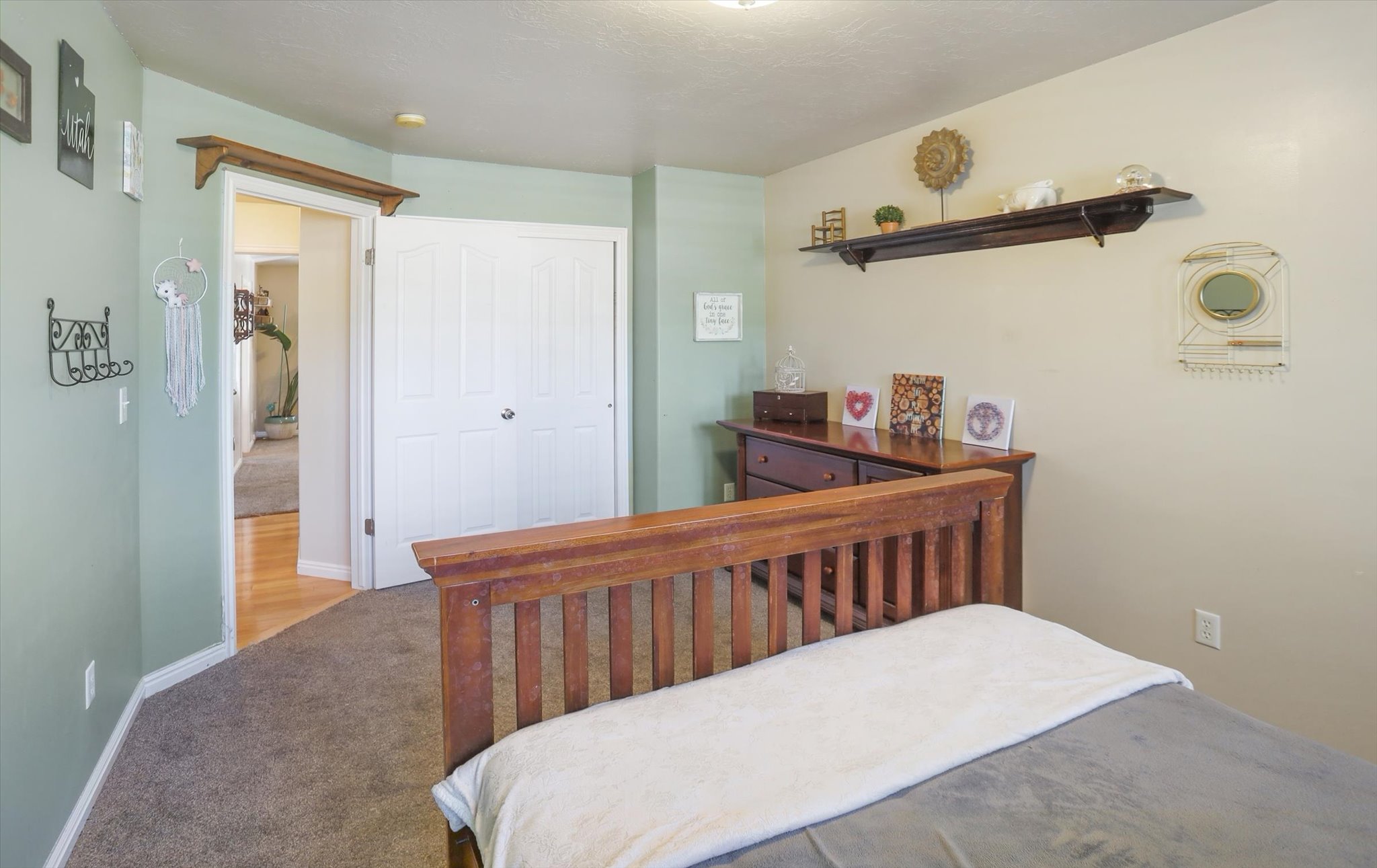 Carpeted room featuring a white bi-fold closet door, a wood-finish bed frame, and a wall-mounted wood-finish shelf