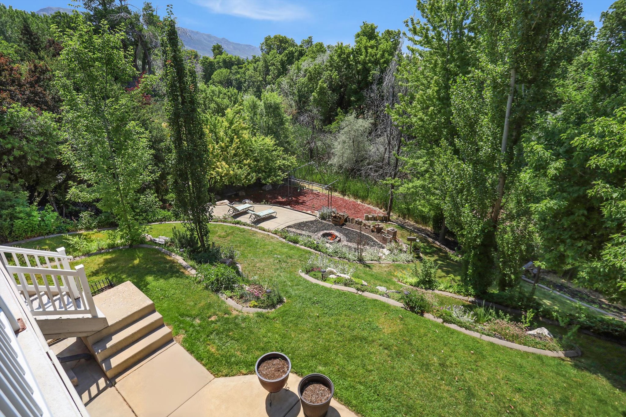 Expansive backyard featuring a manicured lawn, tiered landscaping, and mature trees