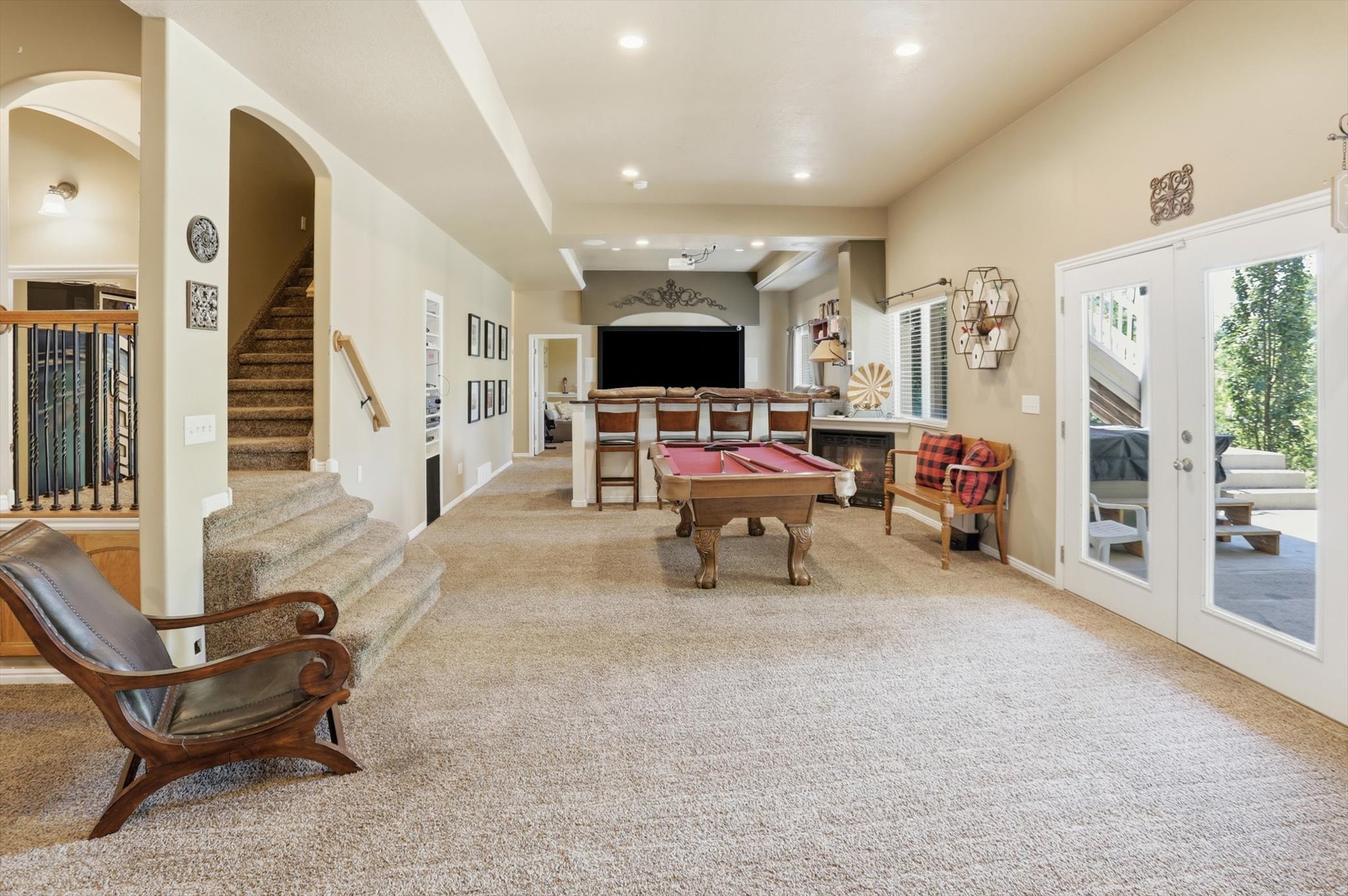 Spacious lower-level entertainment area with neutral carpeting, a built-in wet bar, a fireplace, and double glass doors leading to an outdoor patio