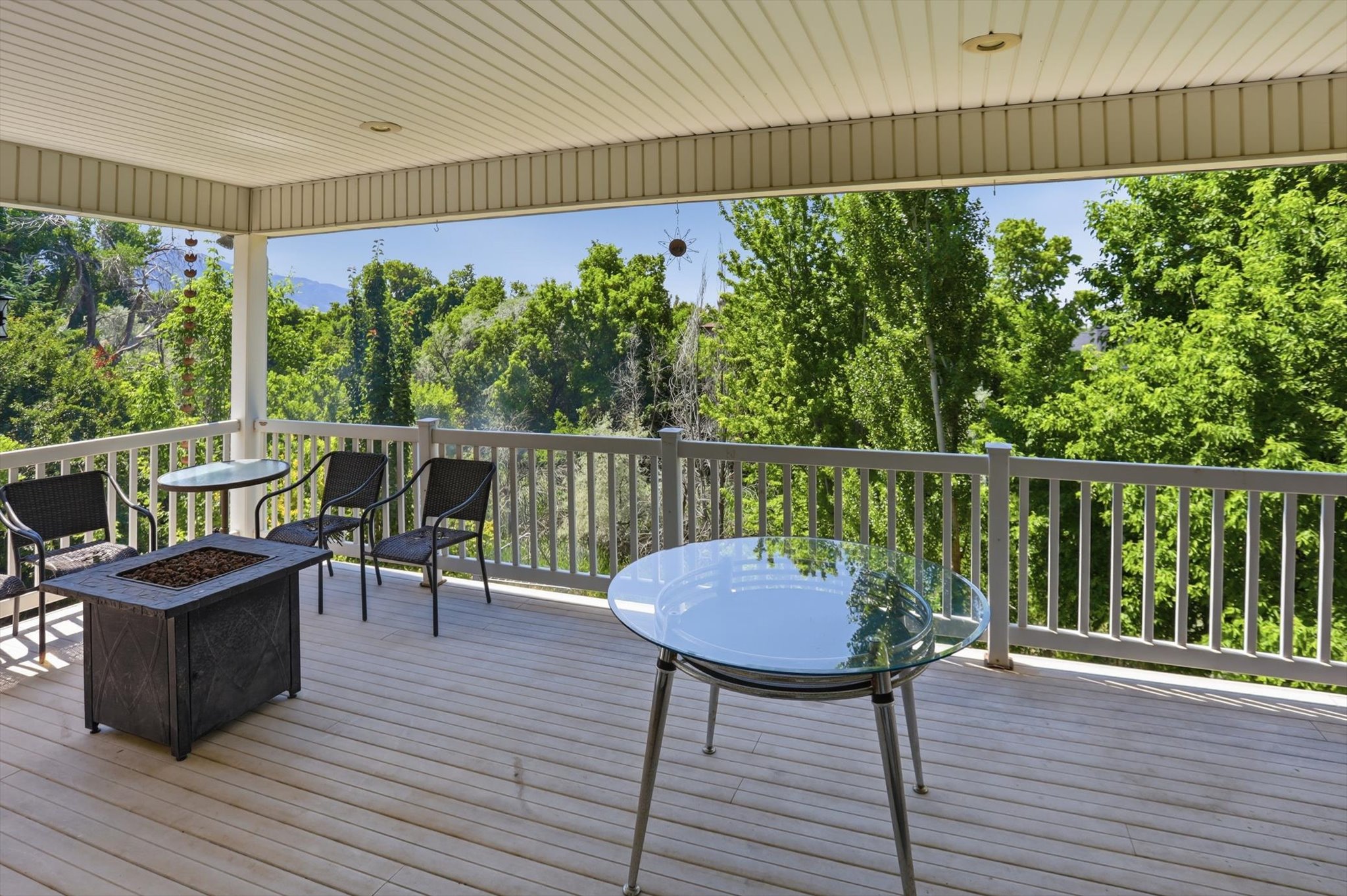 Expansive covered deck featuring wood-finish flooring, white railing, and a built-in fire pit