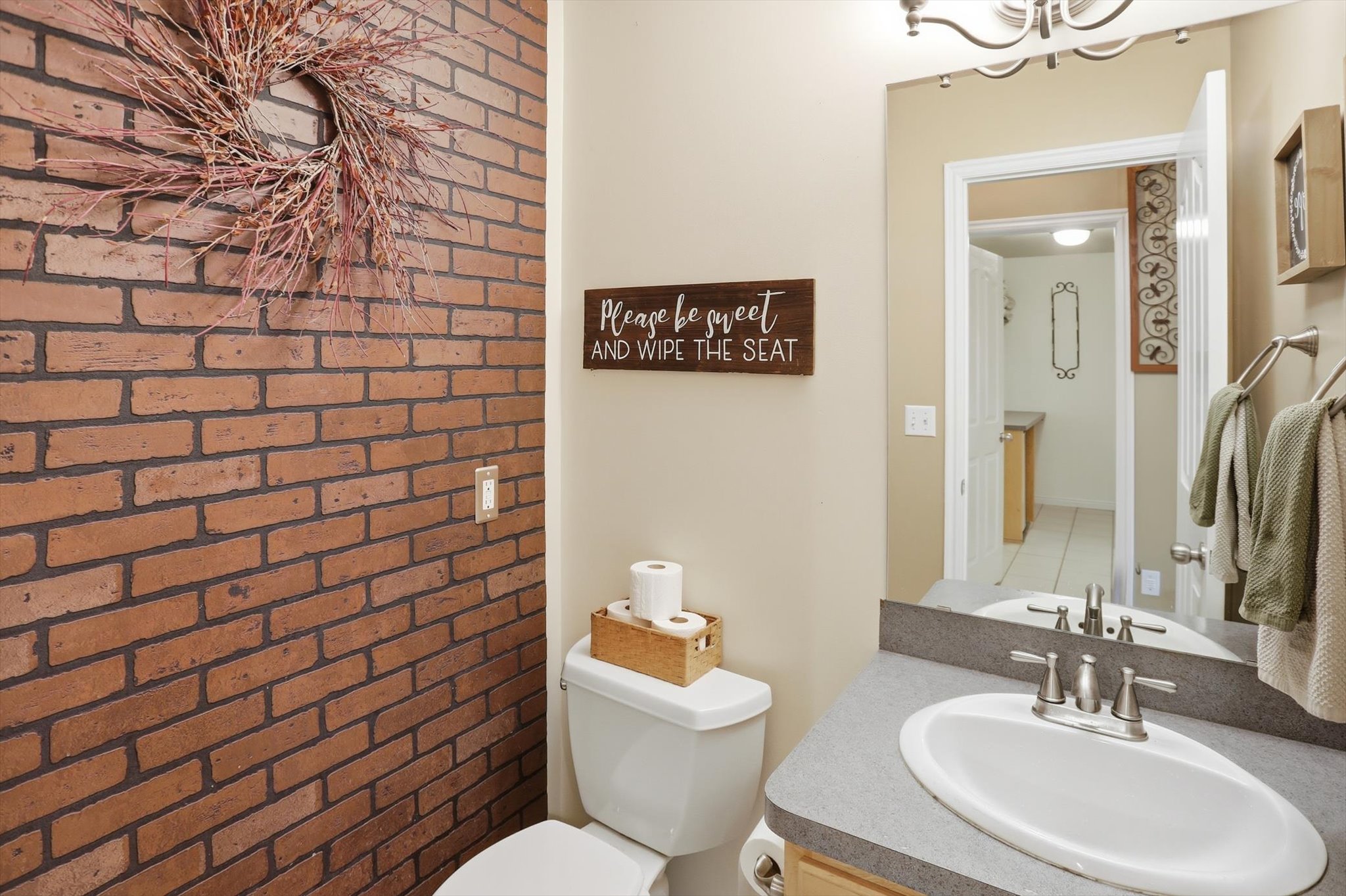 Powder room featuring a brick accent wall, a vanity with a gray countertop, an oval undermount sink, and a two-handle faucet