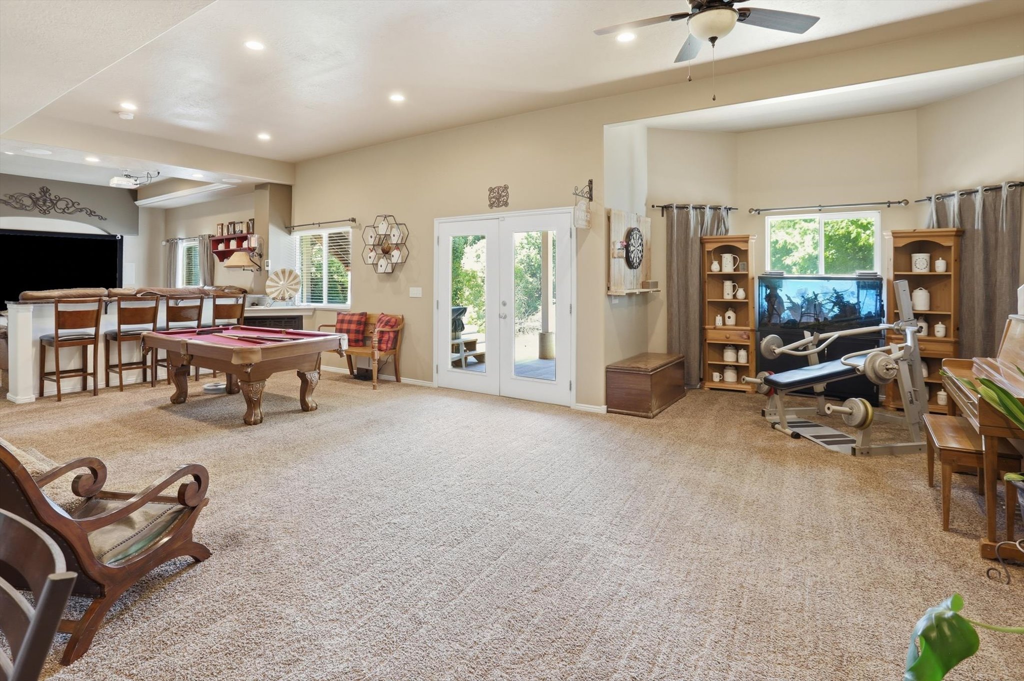 Spacious open-concept room featuring plush carpet flooring, a built-in wet bar with seating, recessed lighting, and a ceiling fan