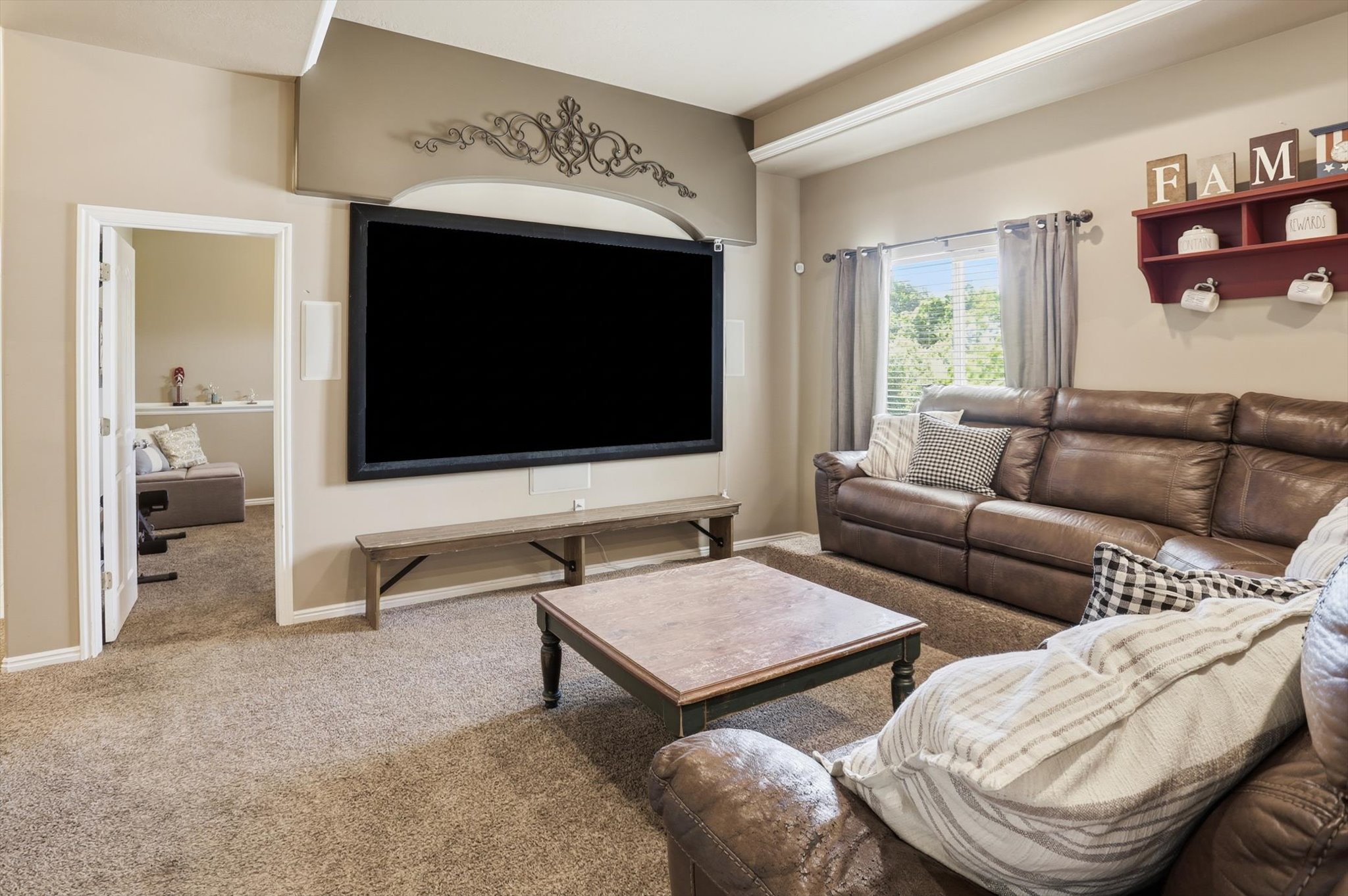 Carpeted living area featuring a large wall-mounted screen with decorative archway, recessed lighting, and a built-in speaker