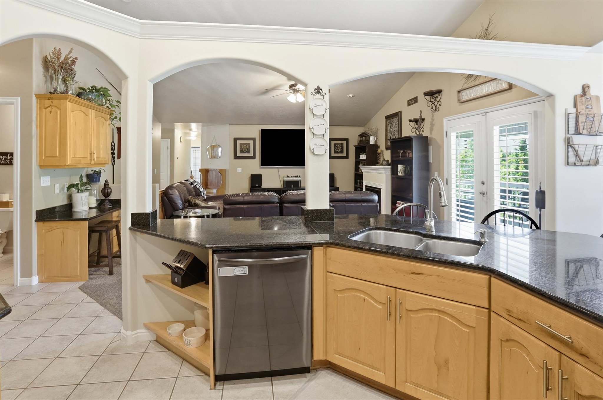 Kitchen featuring a dual basin sink, black granite countertops, light wood cabinetry, and a stainless steel dishwasher