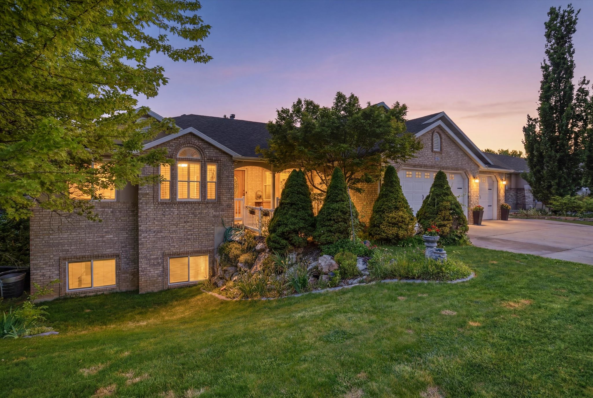 Brick facade residence featuring multiple garage bays, an arched window, and established landscaping