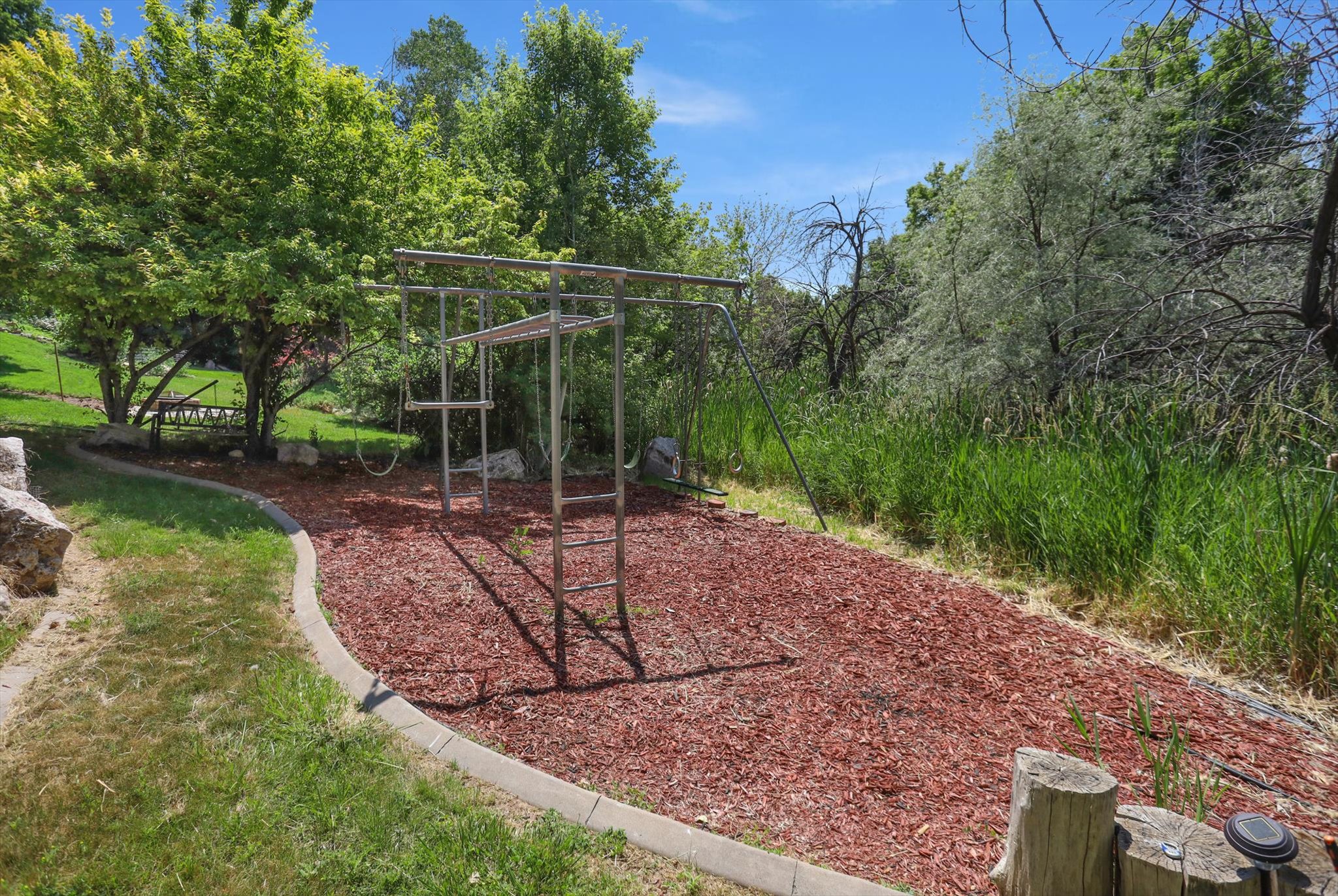 Outdoor play area featuring a metal playset, ground cover of red wood chips, and a concrete border