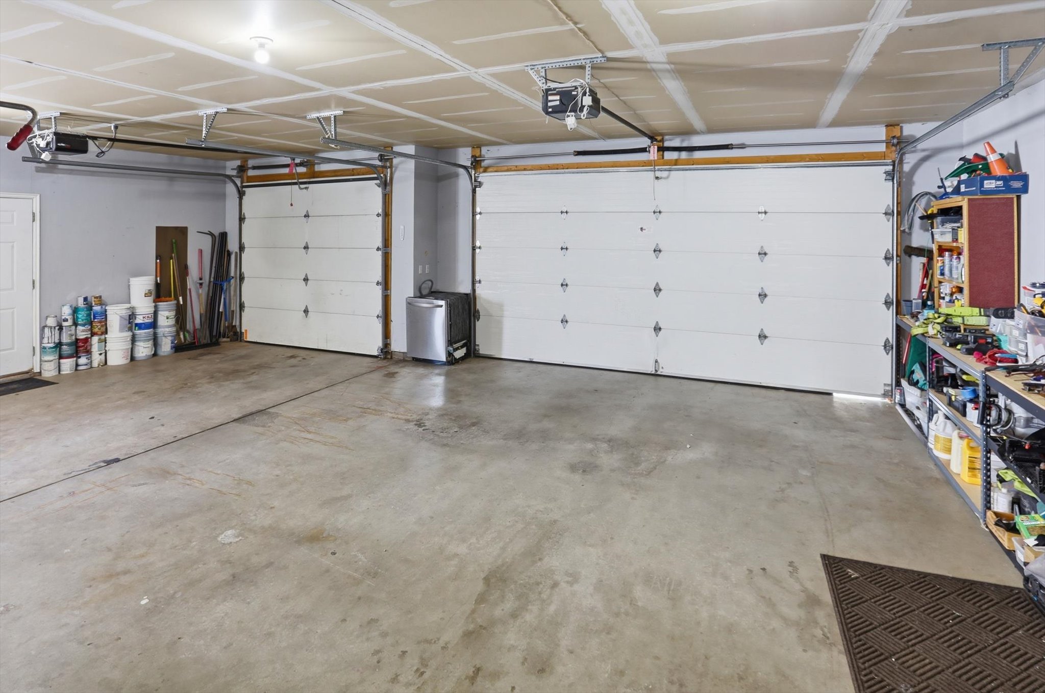 Spacious two-car garage featuring concrete flooring, two white panel garage doors with automatic openers, and overhead lighting