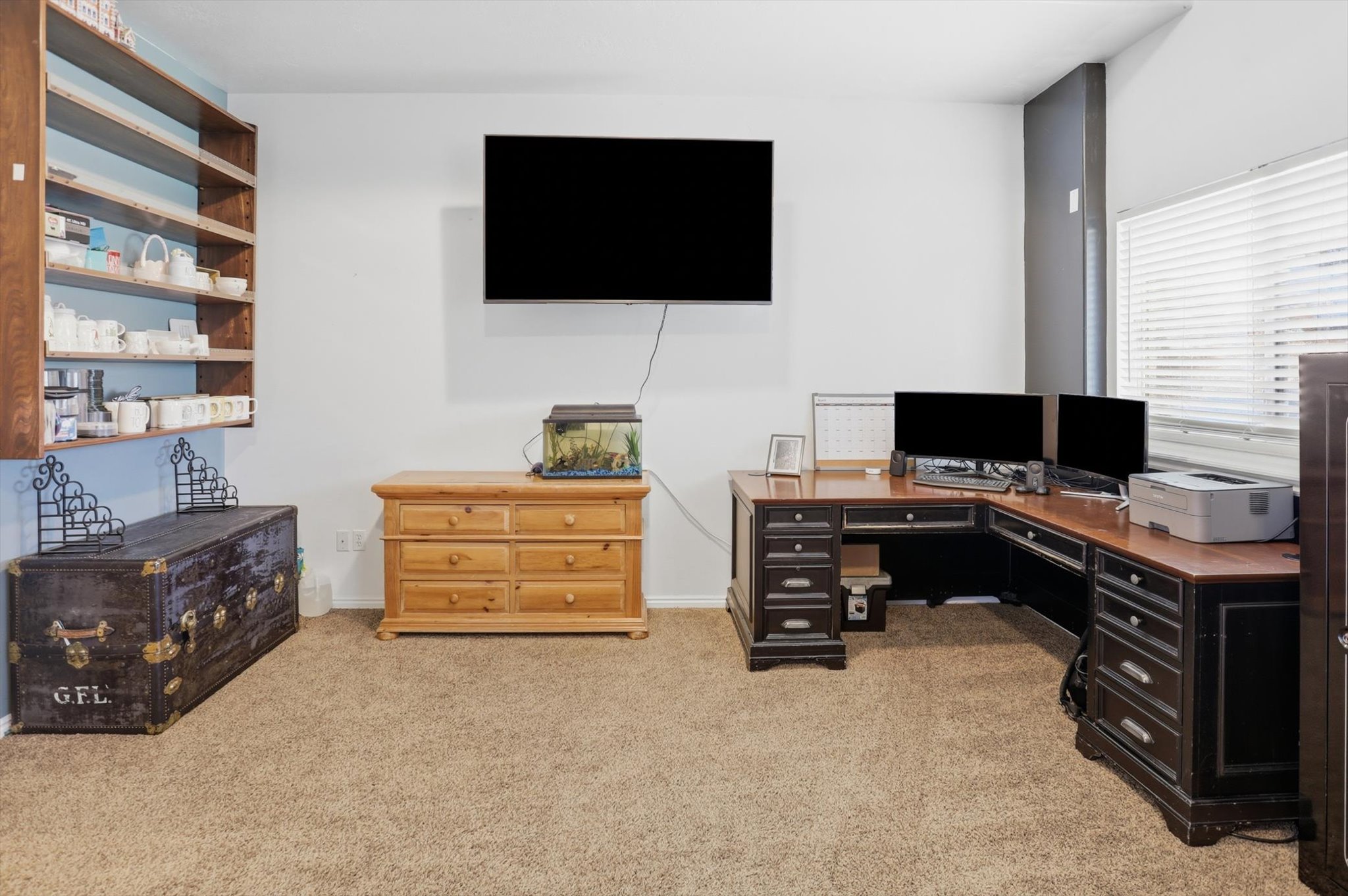 Carpeted room featuring a built-in wooden shelving unit, a wall-mounted display, and horizontal window blinds