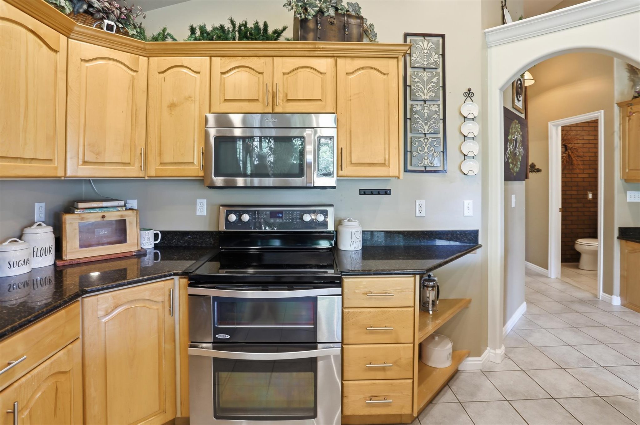Light wood cabinetry with stainless steel appliances, dark stone countertops, and tile flooring