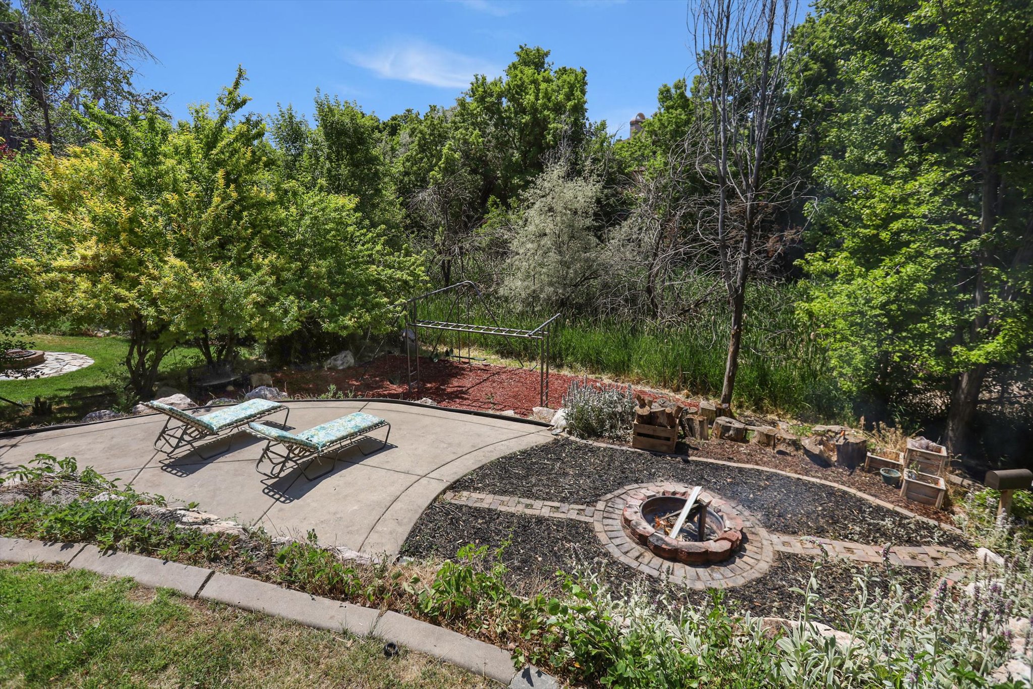 Outdoor entertainment area featuring a circular concrete patio, a brick-ringed fire pit, and tiered landscaping