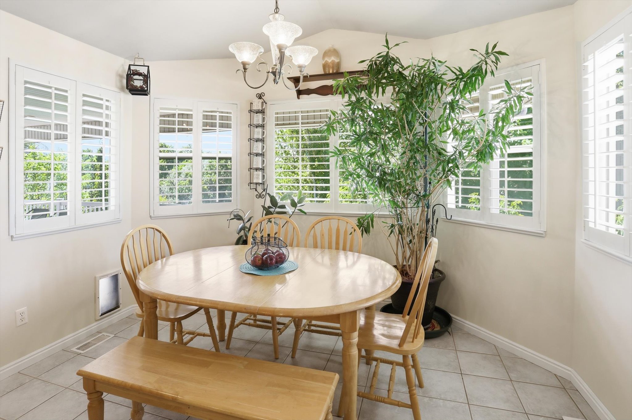 Dining area featuring multiple windows with white plantation shutters, neutral-toned walls, a decorative chandelier, and tile flooring