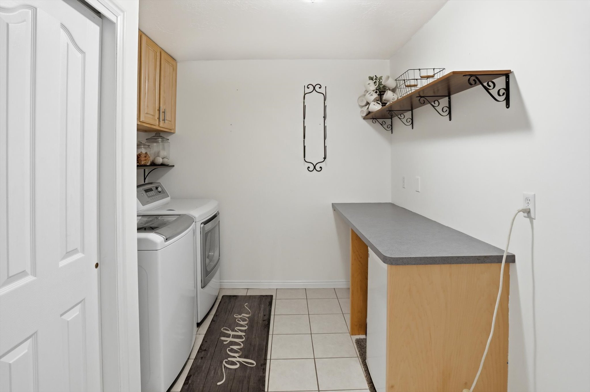 Dedicated laundry area featuring a built-in counter, wood-finish shelving with decorative brackets, and overhead cabinetry