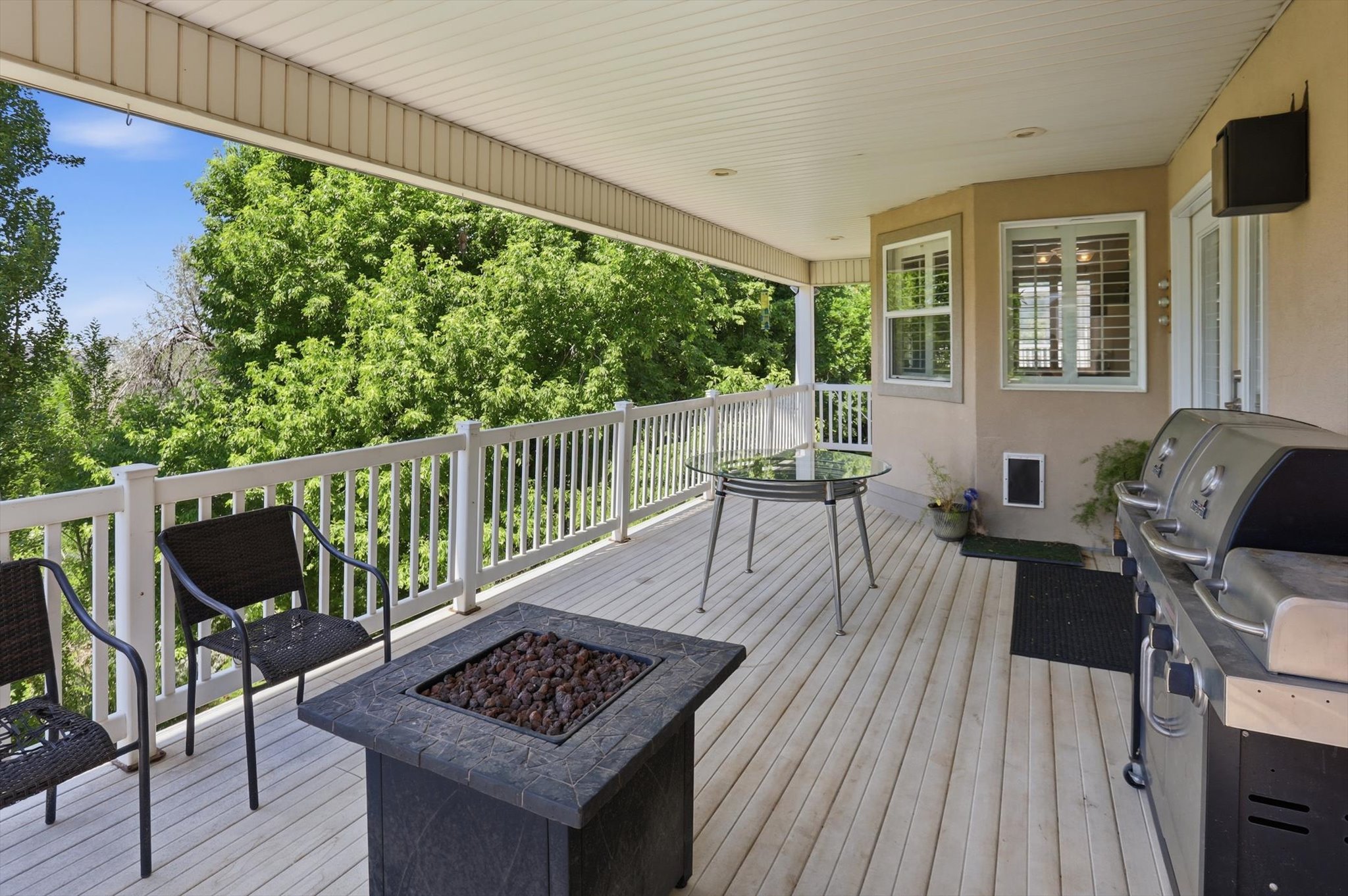 Spacious covered outdoor deck with light wood-finish flooring, white railing, and exterior wall access