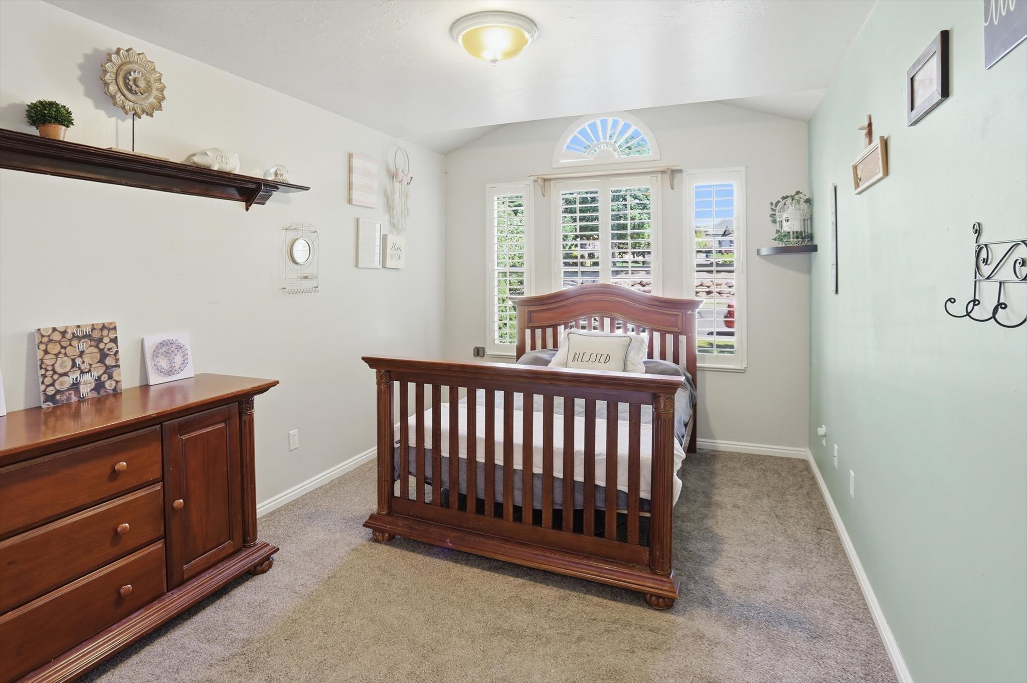 Vaulted ceiling with an arched window featuring plantation shutters, neutral carpeting, and baseboard molding