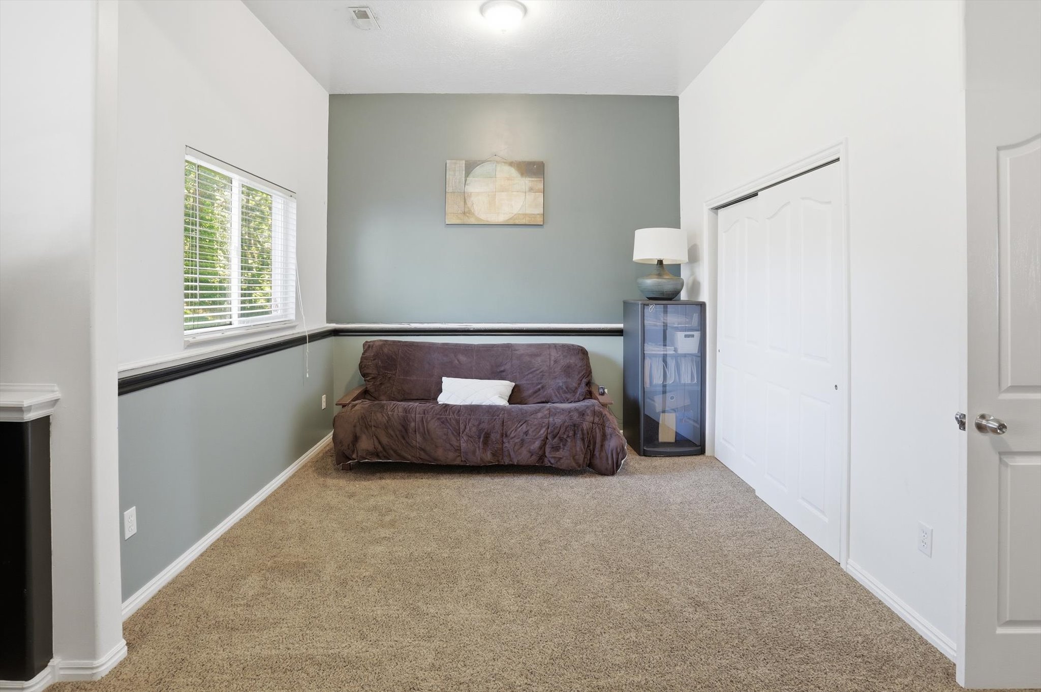 Carpeted room featuring a window with blinds, a two-tone wall treatment, and a white bi-fold closet door
