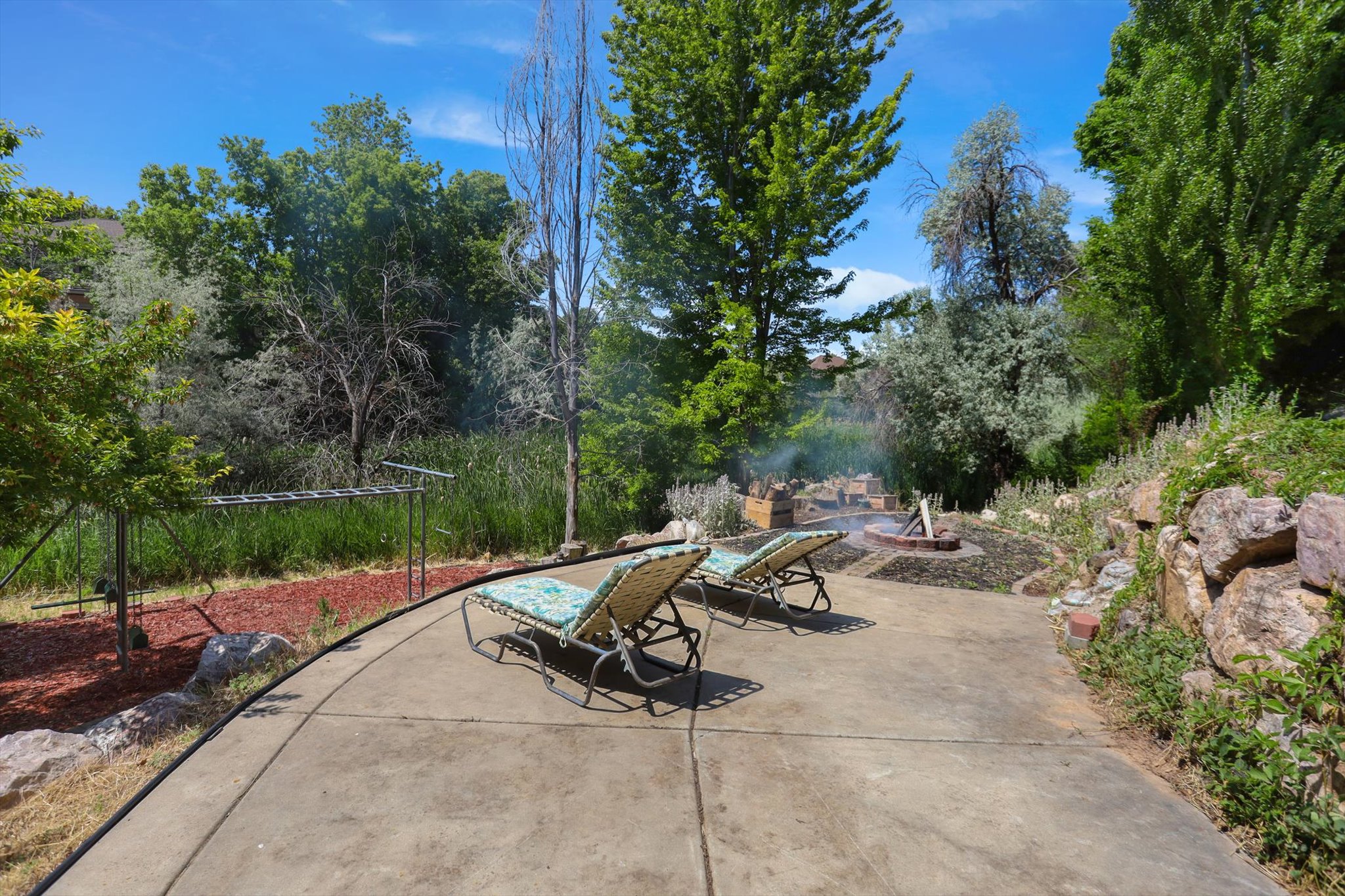 Concrete patio with a built-in fire pit, surrounded by natural landscaping and mature trees