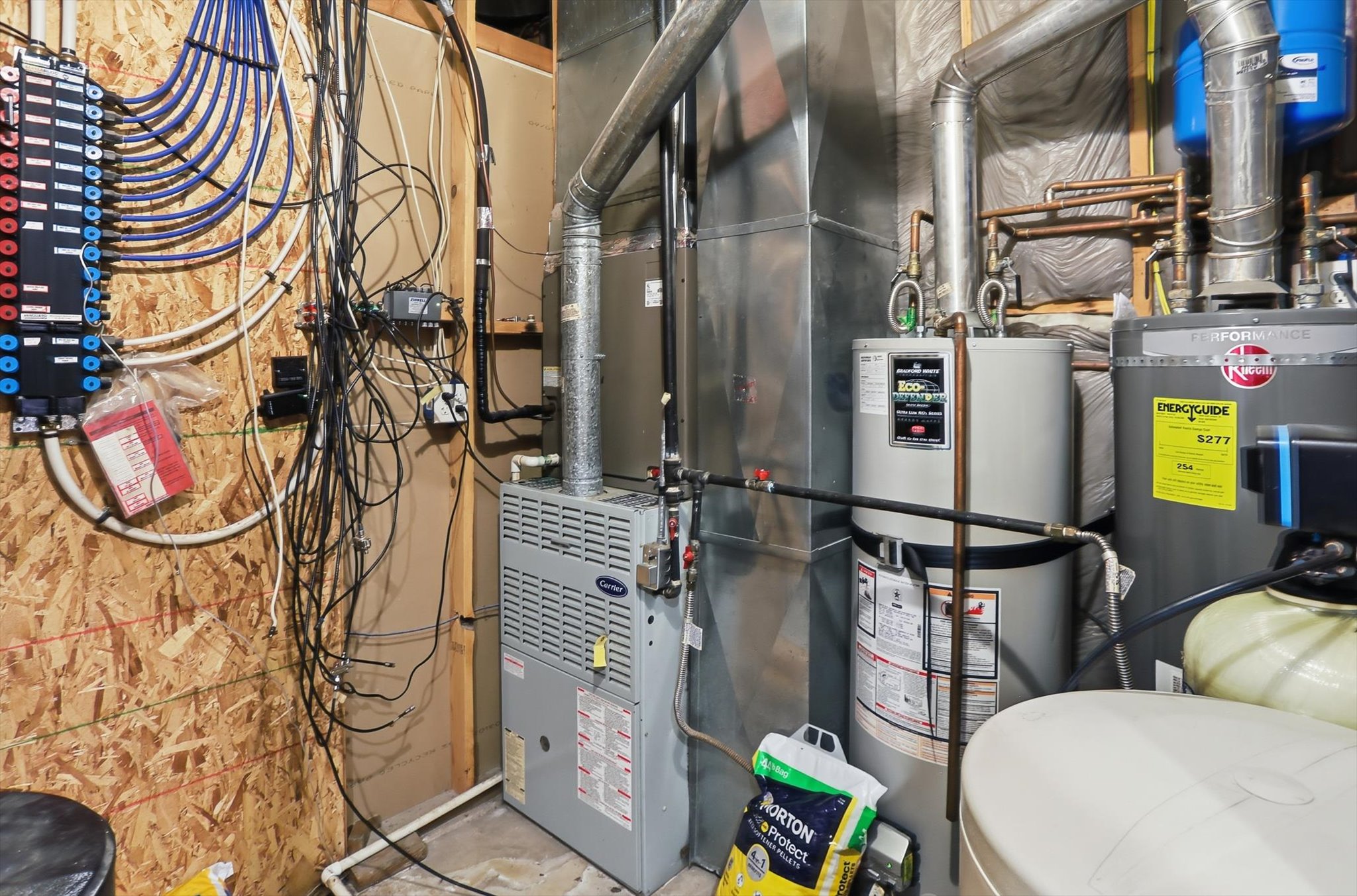 Dedicated utility space featuring a forced-air furnace, two water heaters, a water softener system, and a comprehensive manifold plumbing system