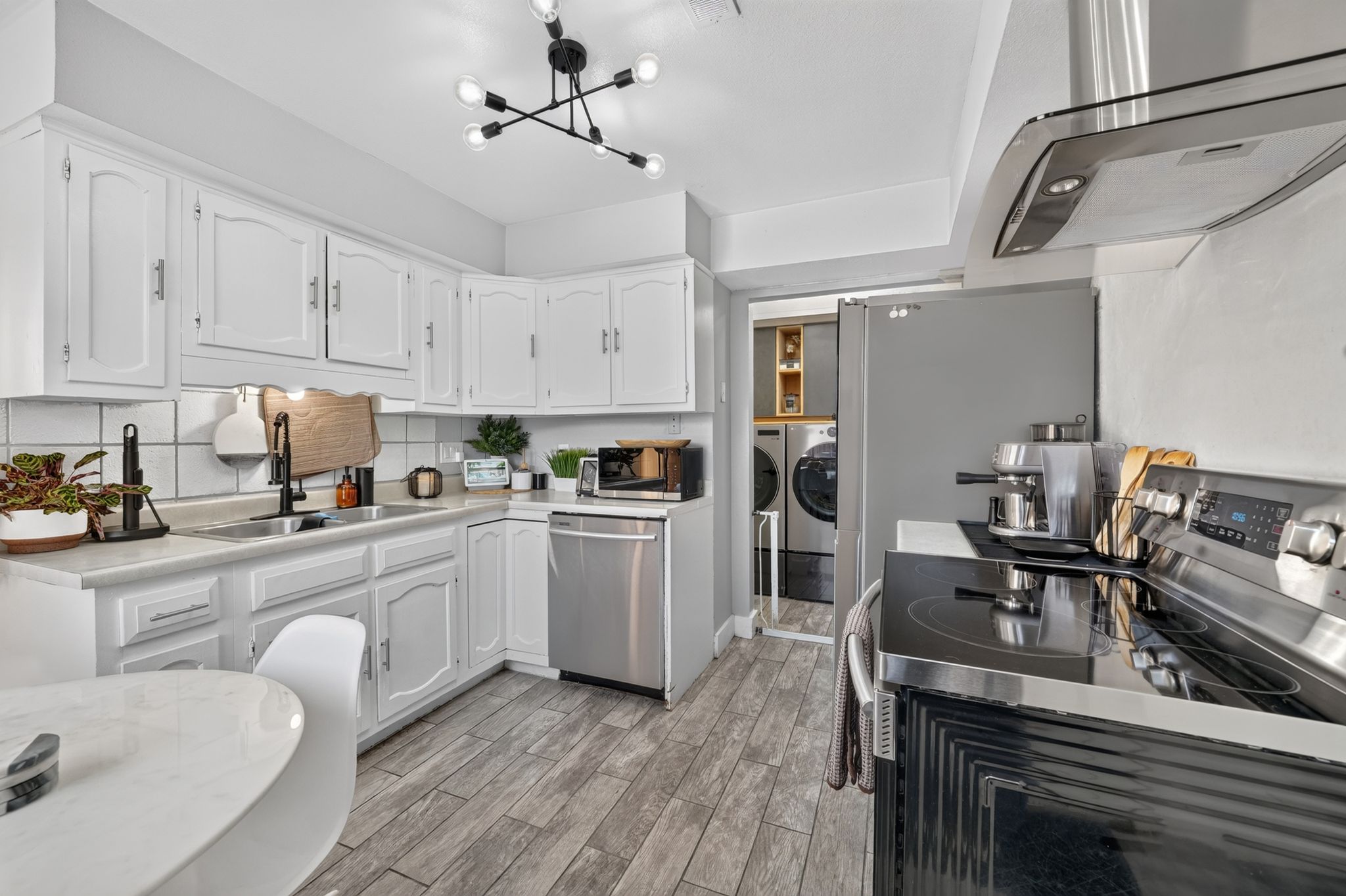 Kitchen featuring white cabinetry, wood-finish flooring, stainless steel appliances, and a contemporary light fixture