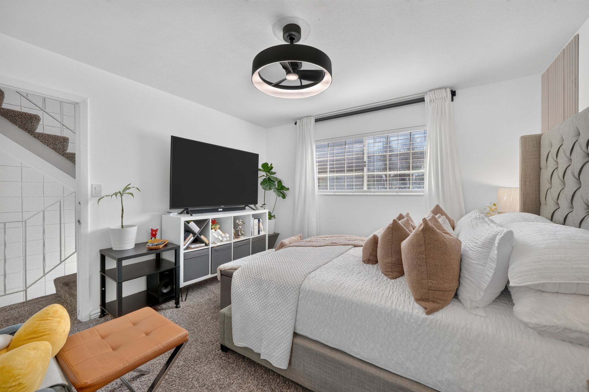 Carpeted bedroom with a modern ceiling light fixture, white walls, and a window featuring white blinds