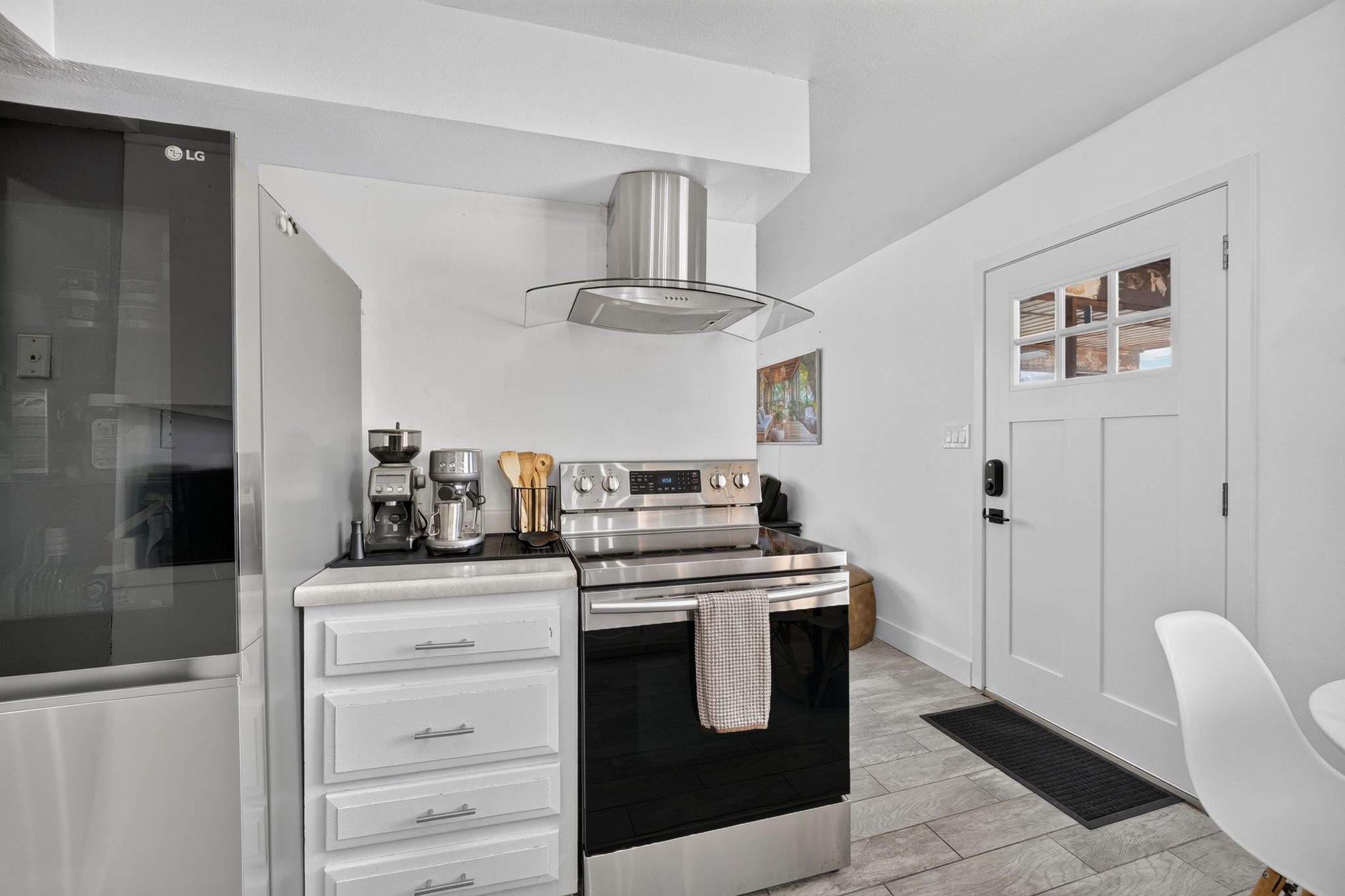 Kitchen area featuring stainless steel appliances, a range with an overhead vent hood, white cabinetry with silver hardware, and light-toned flooring