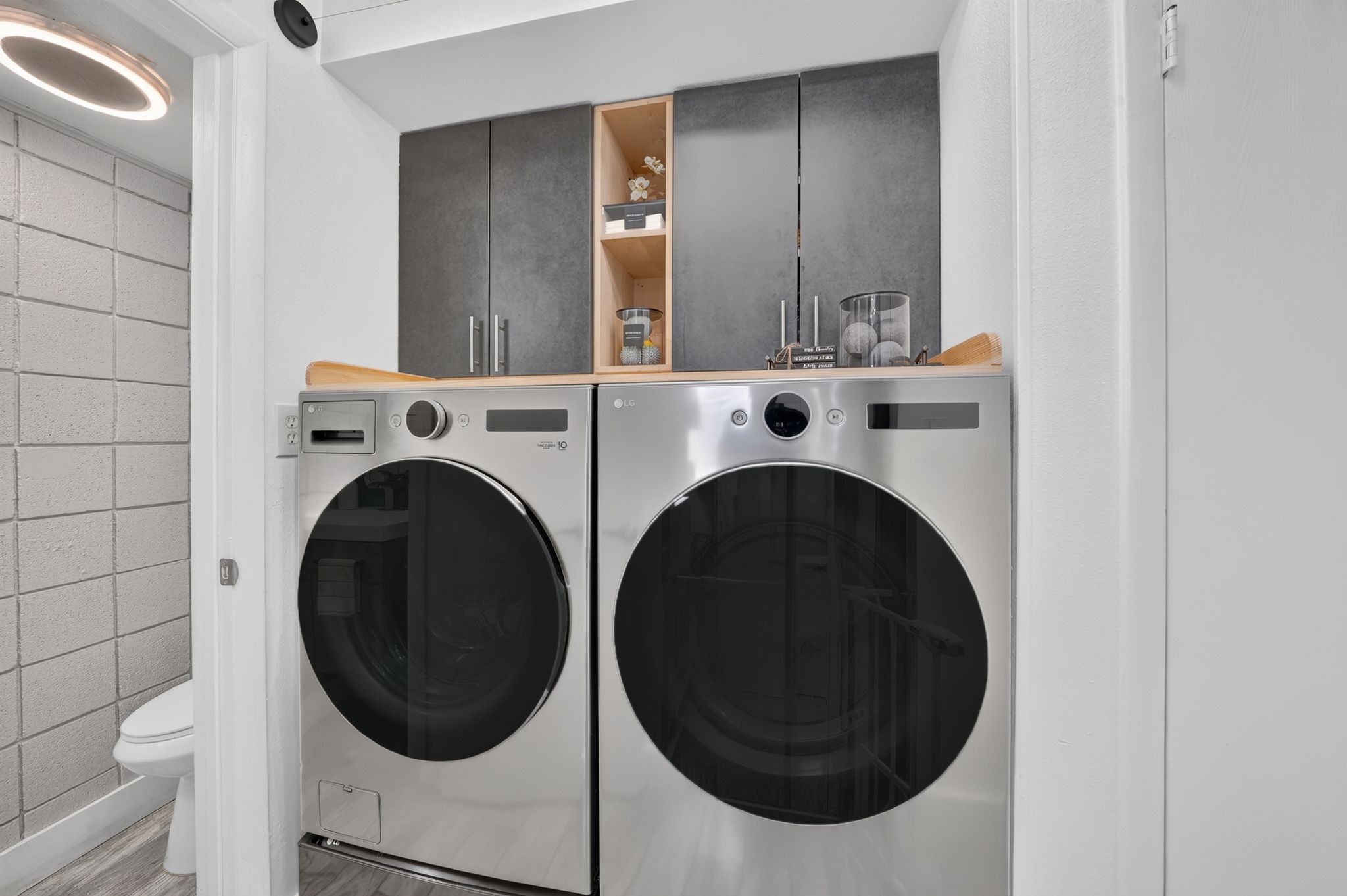 Dedicated laundry area featuring a wood-finish countertop, dark gray cabinetry, and open shelving
