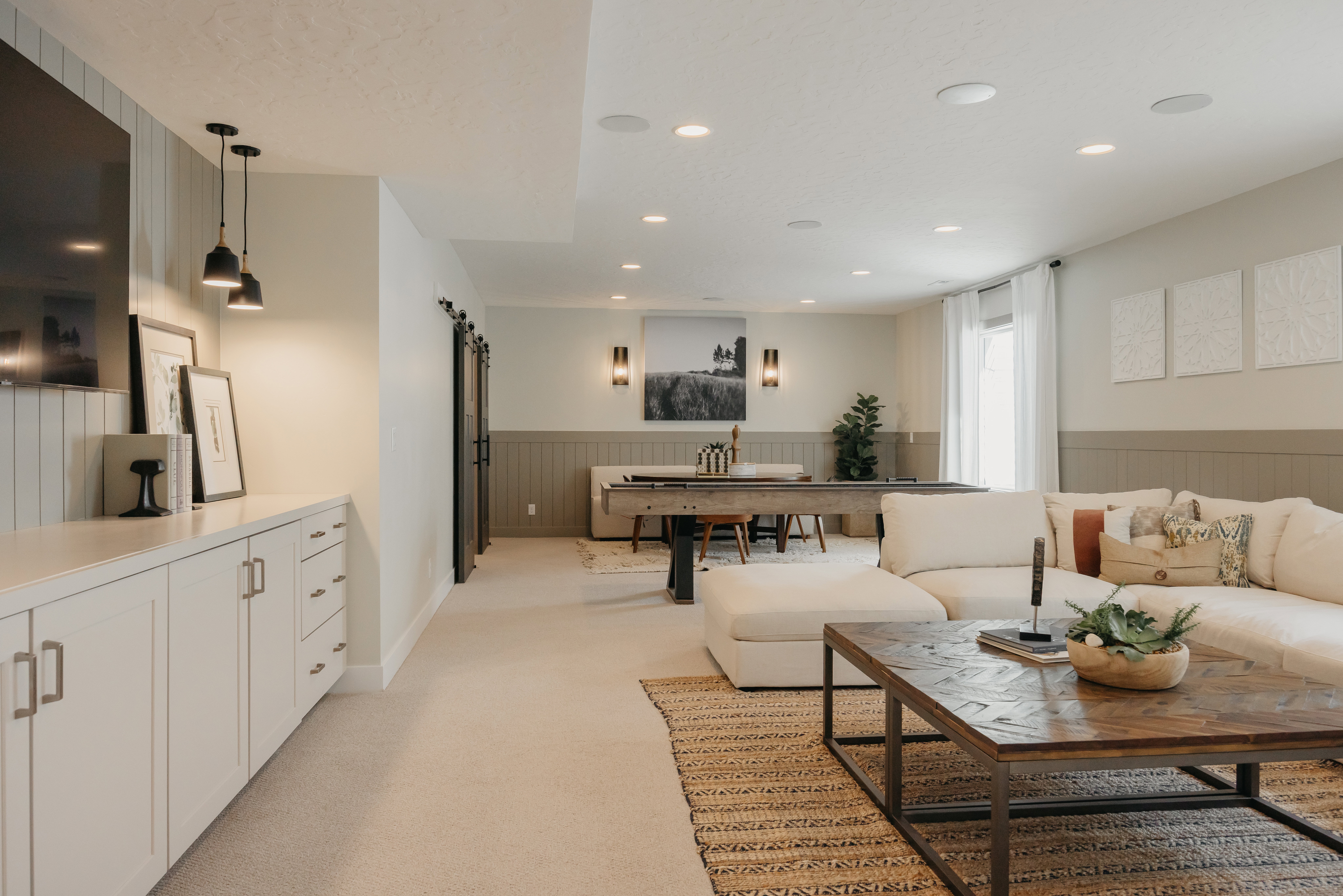 Spacious recreation area featuring recessed lighting, a built-in media cabinet with countertop, two dark sliding barn doors, and wainscoting