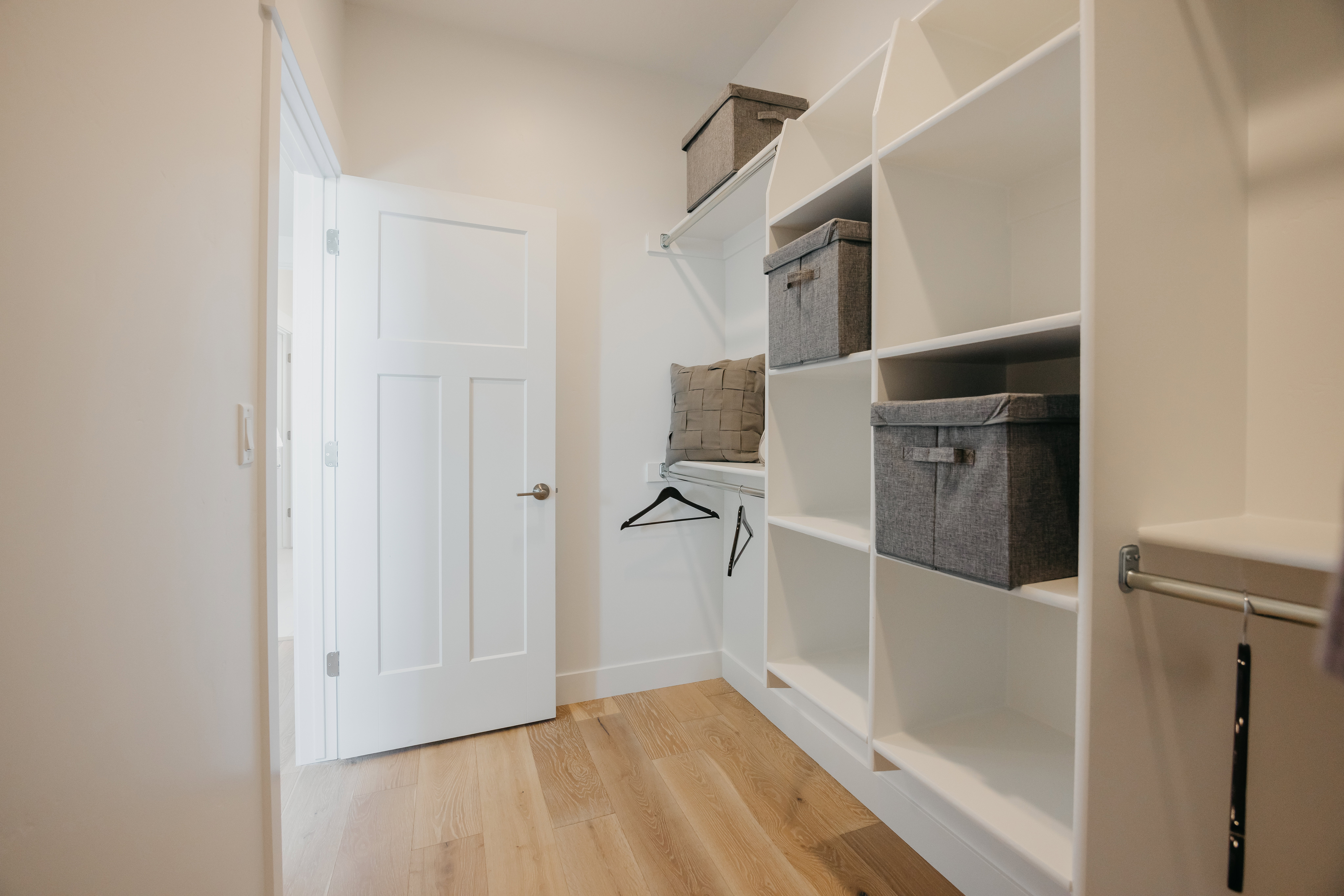 Walk-in closet featuring light wood-finish flooring, white shelving, and hanging rods