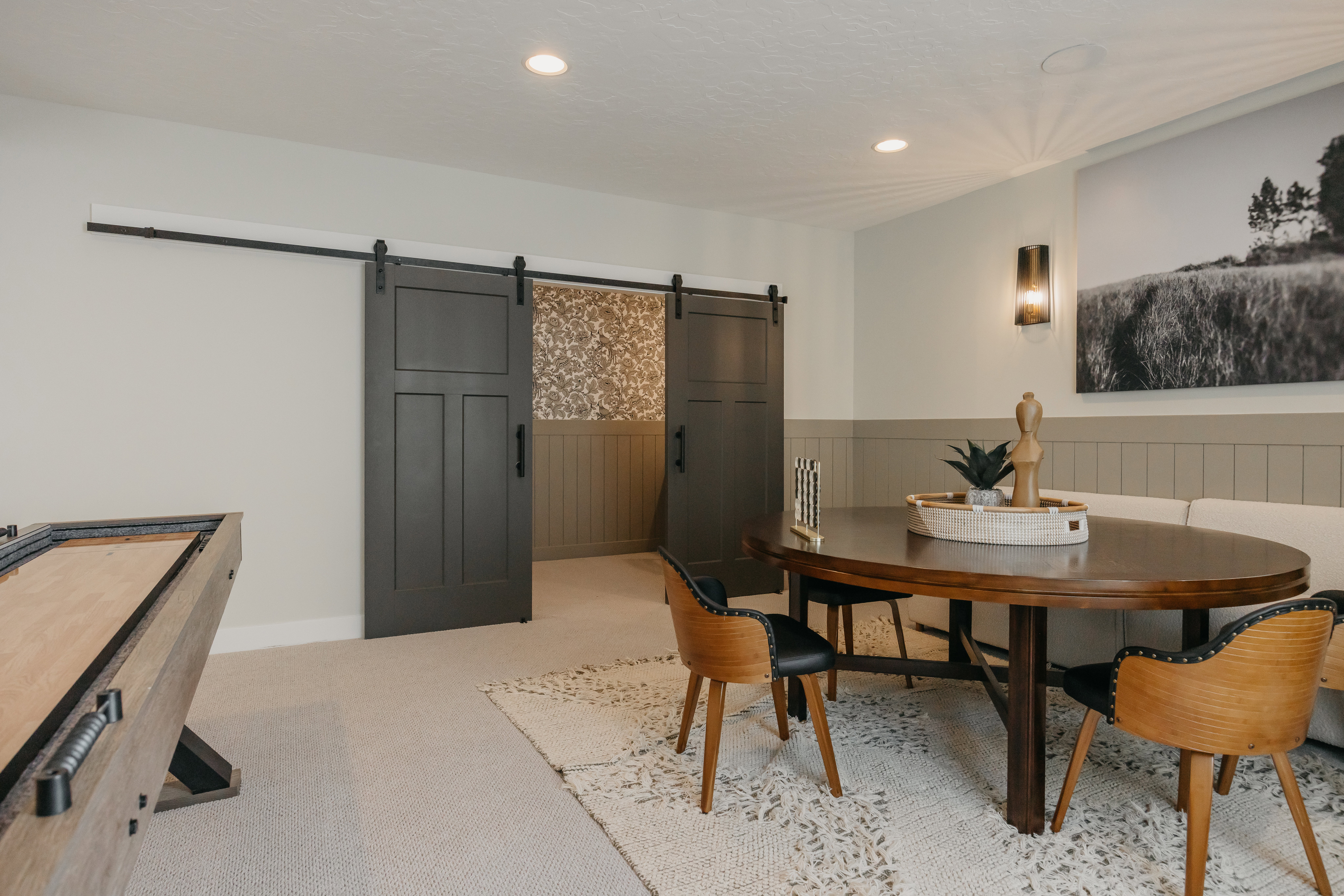 Double barn doors with black hardware, recessed ceiling lighting, and wainscoting with a painted wall panel