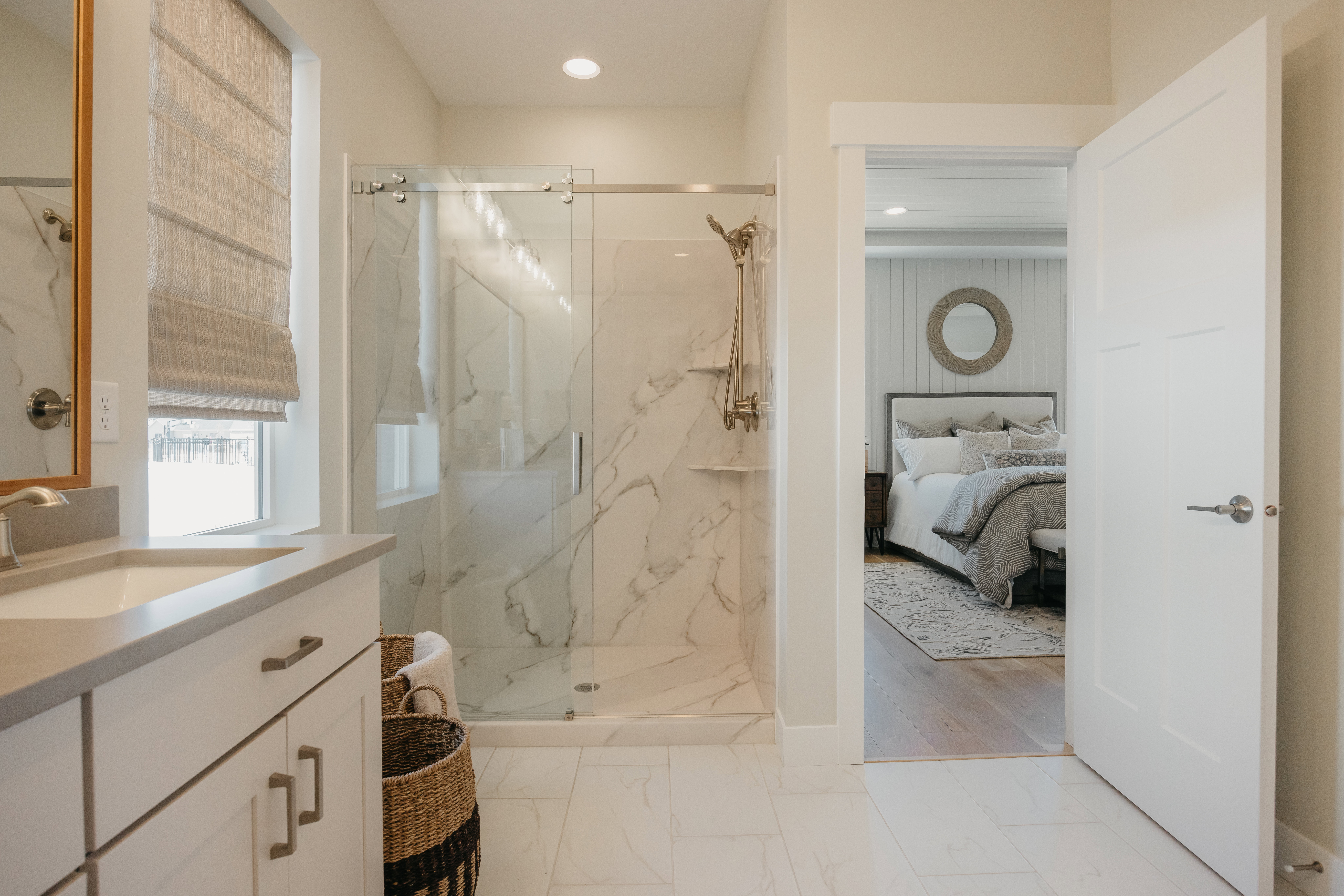 Spacious bathroom featuring a frameless glass shower enclosure with marble-look tile surround, a single vanity with a light-toned countertop, and white cabinetry