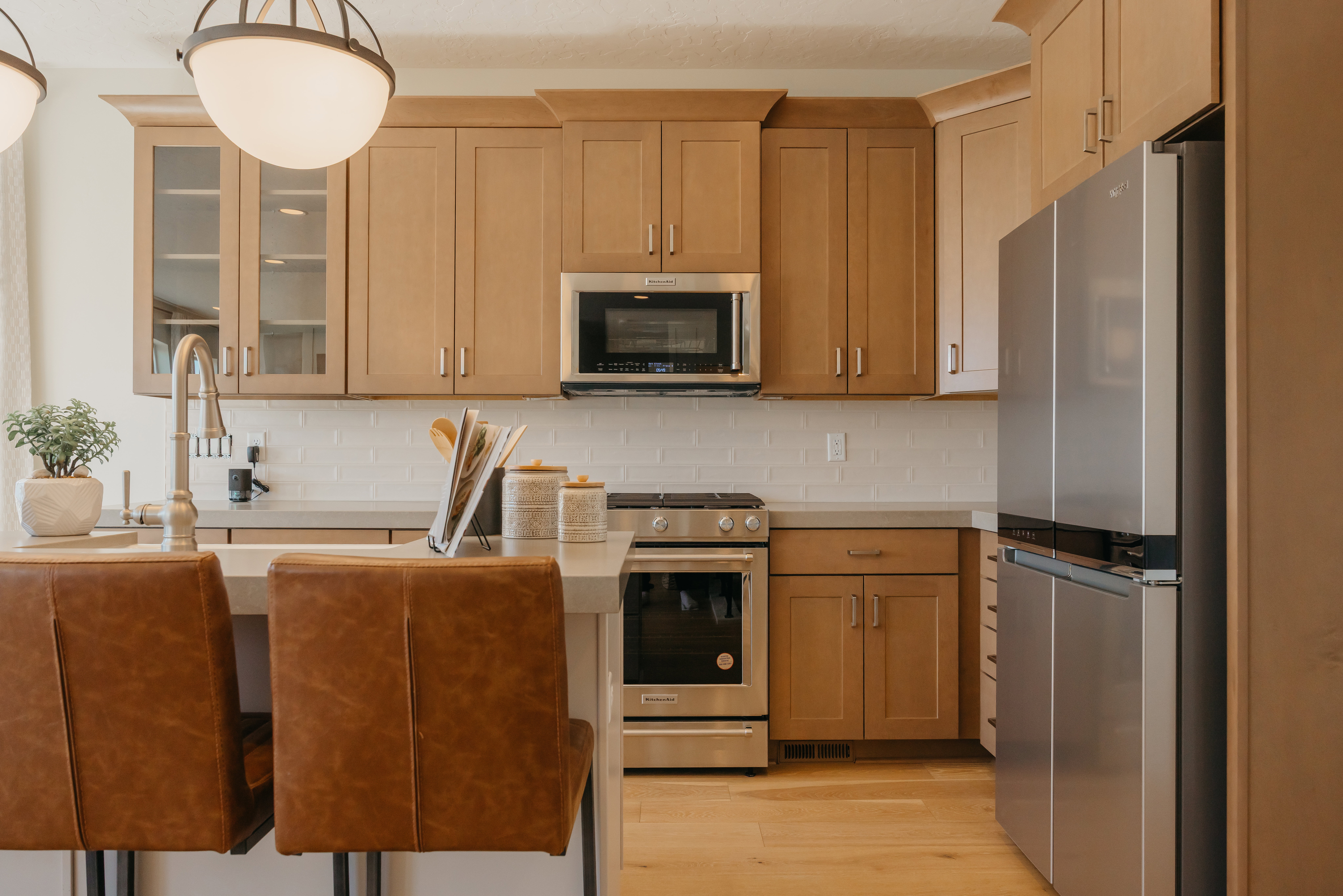 Kitchen featuring light wood cabinetry, stainless steel appliances, a subway tile backsplash, and a central island with an undermount sink