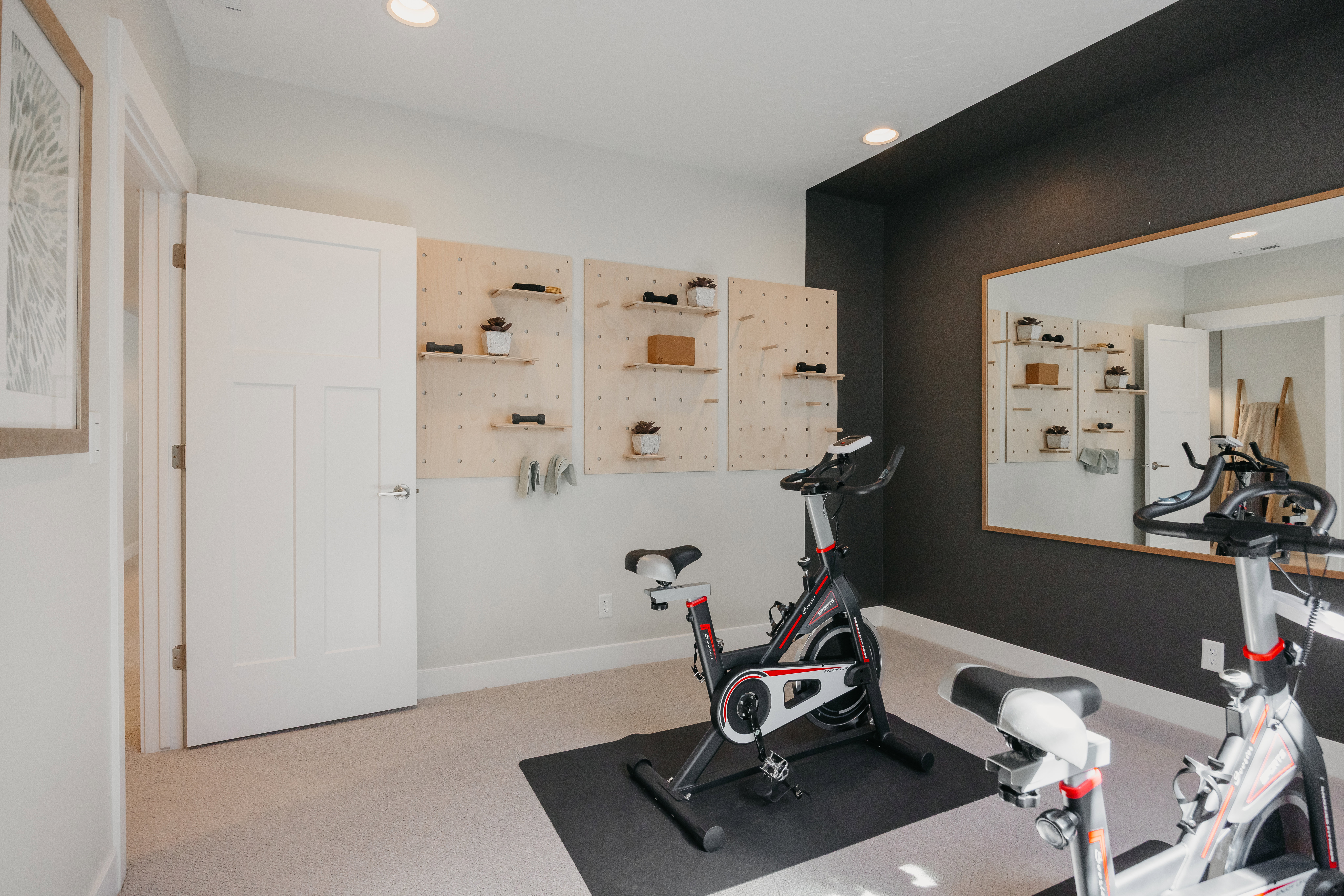 Carpeted room featuring recessed lighting, a dark accent wall with a large framed mirror, and light-colored walls with built-in pegboard shelving