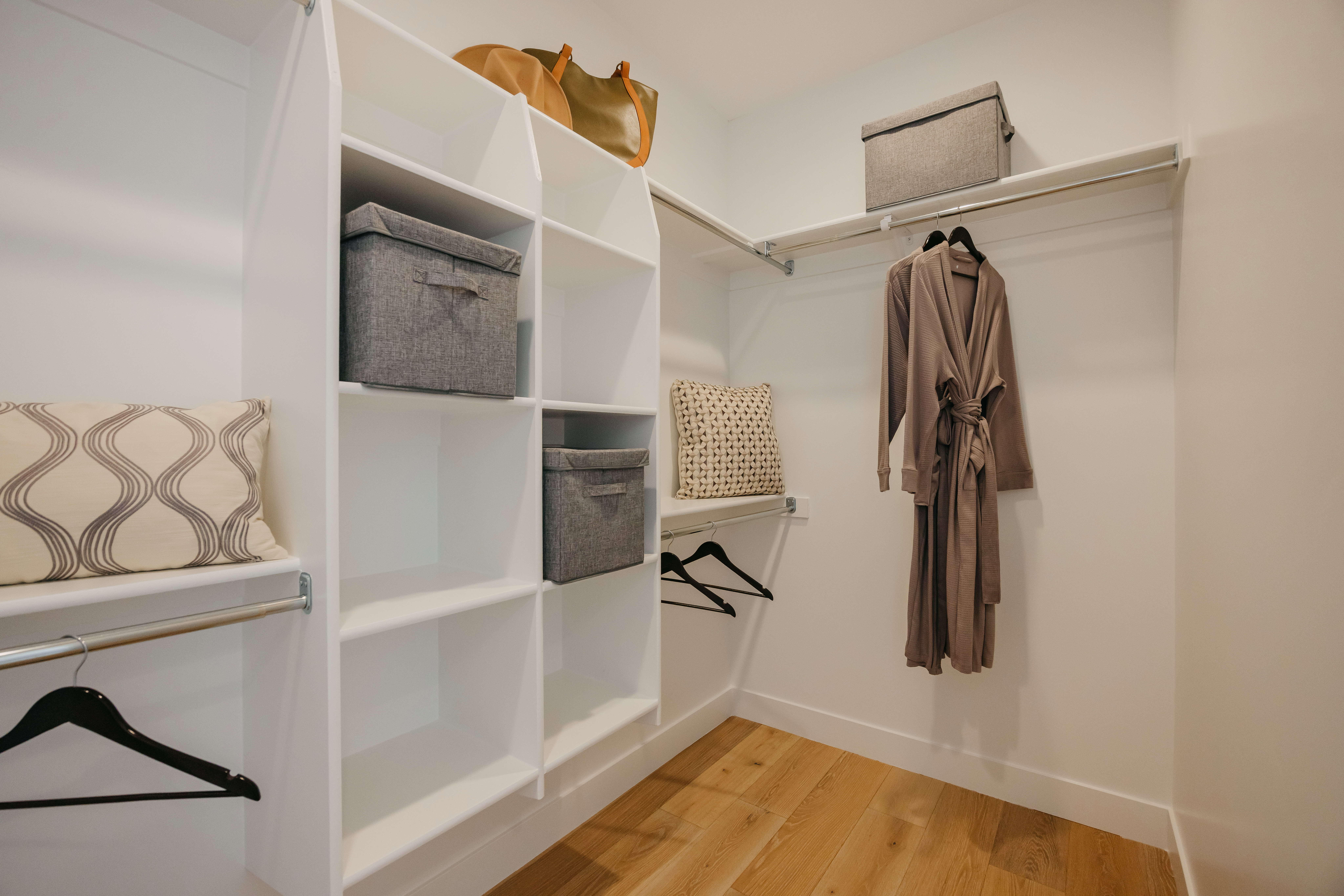 White walk-in closet featuring extensive built-in shelving, multiple hanging rods, and wood-finish flooring
