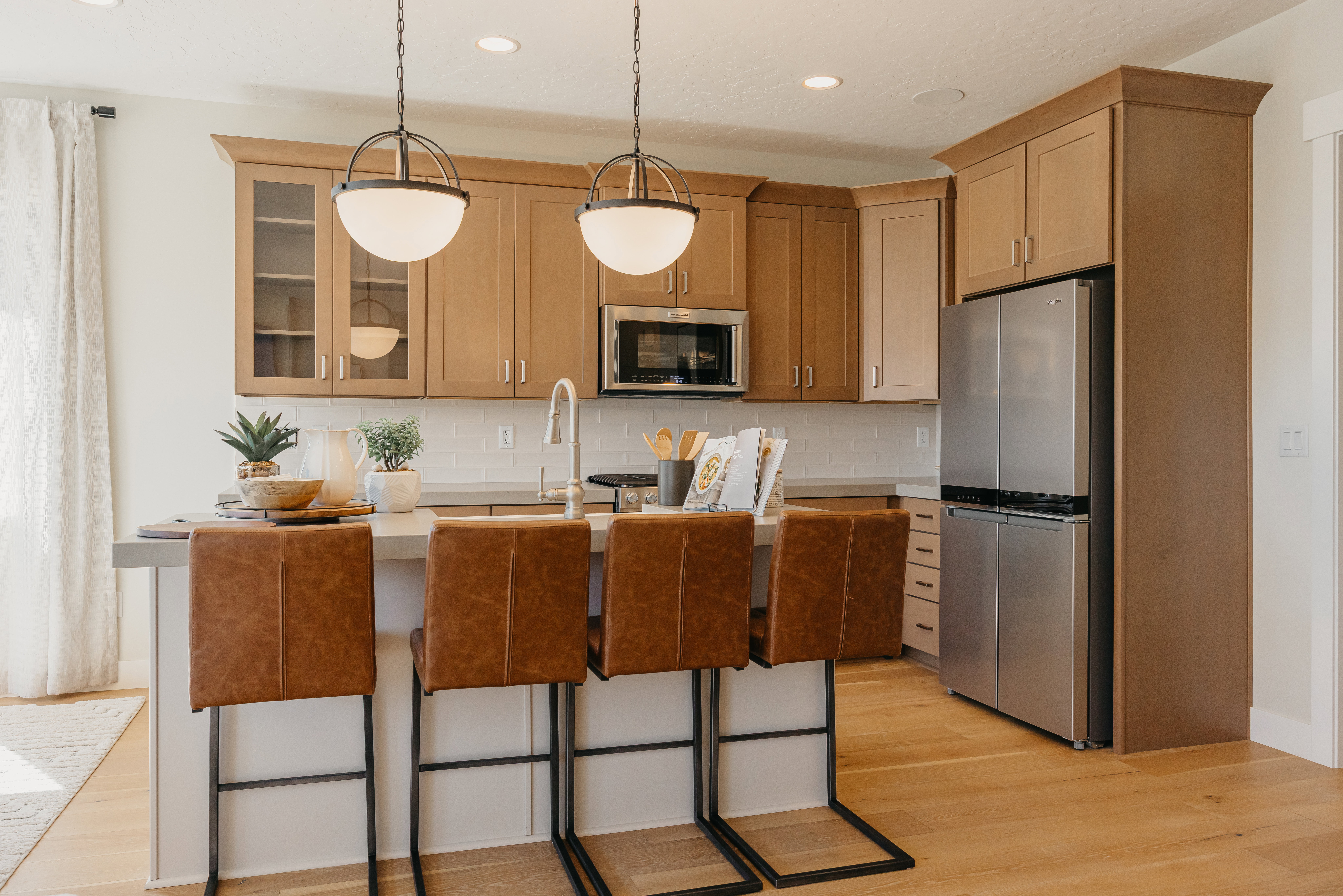Contemporary kitchen featuring wood-finish flooring, light-toned cabinetry, stainless steel appliances, a center island with seating, and pendant lighting