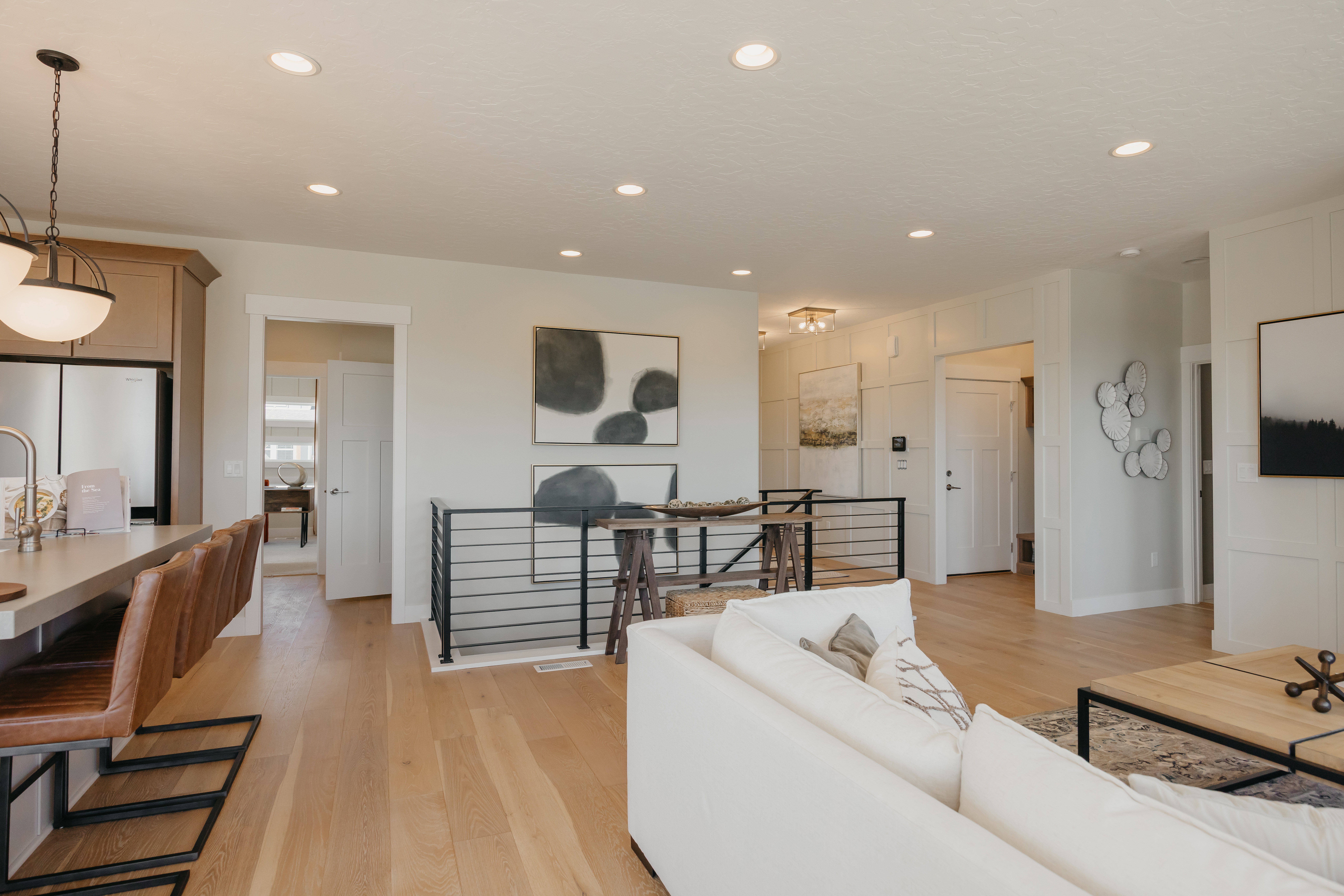 Open-concept living area featuring light wood-finish flooring, recessed lighting, and a modern horizontal metal railing