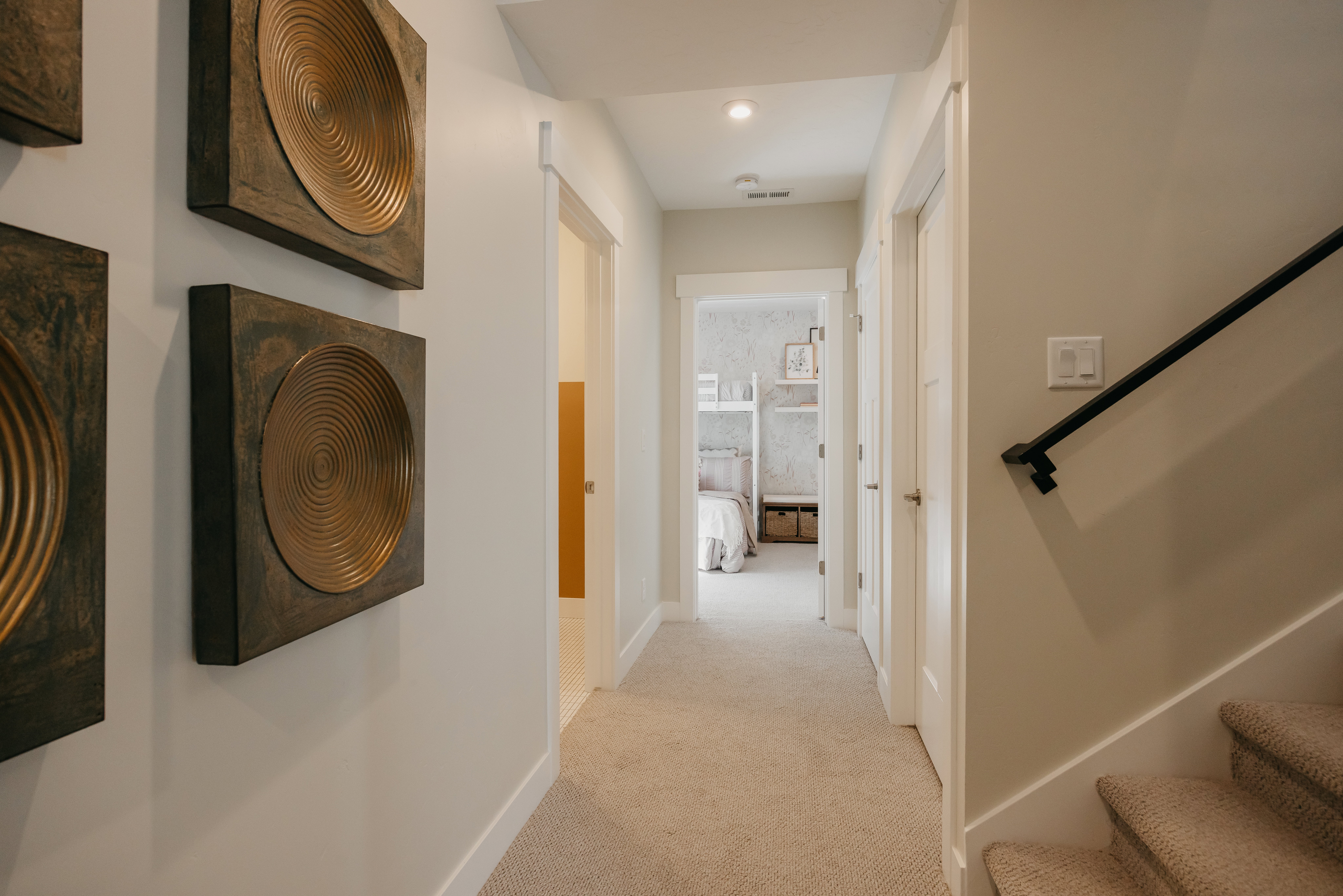 Carpeted hallway with painted walls, recessed lighting, white trim, and a black wall-mounted handrail along the carpeted stairway