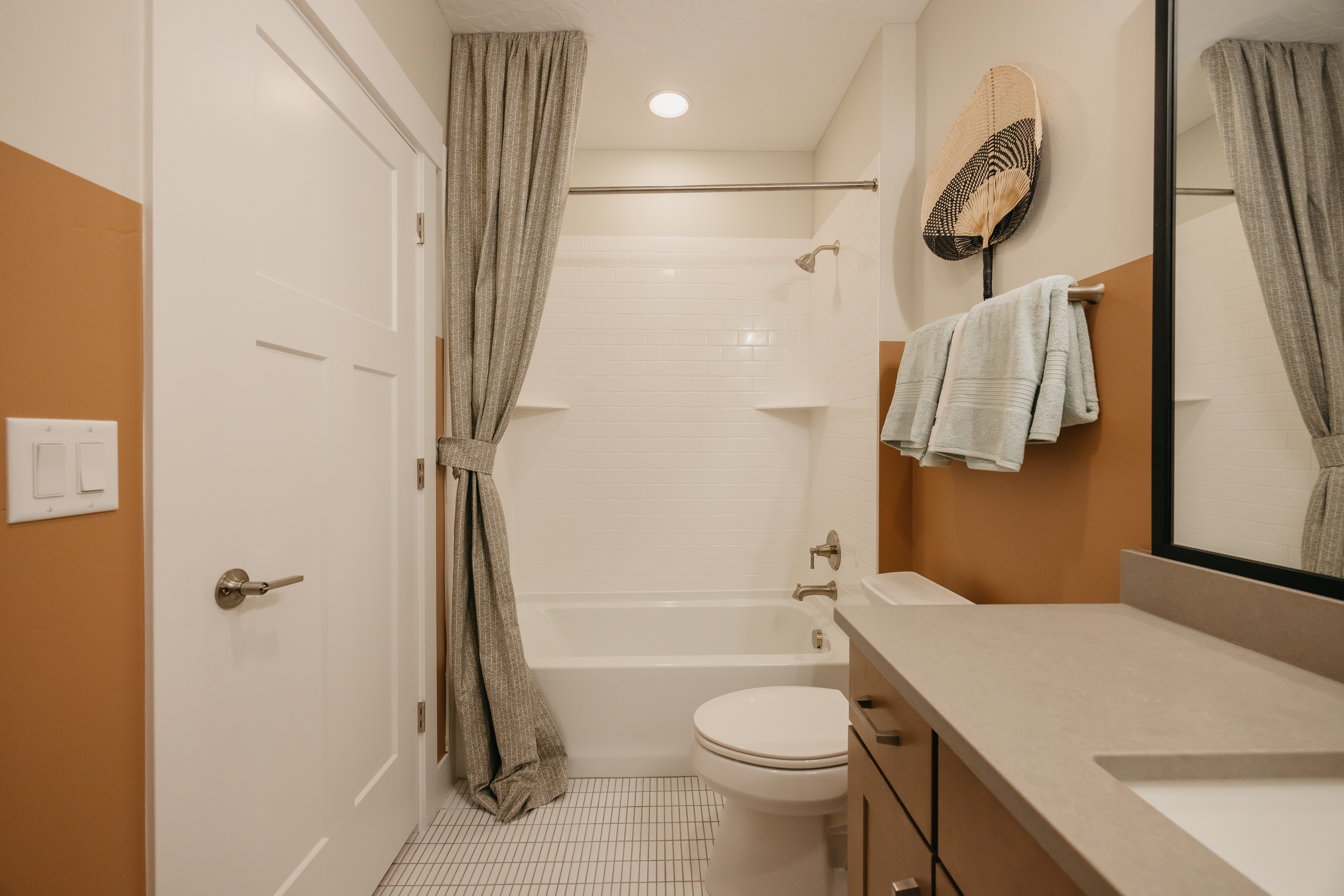 Bathroom featuring a built-in tub and shower combination with subway tile surround, a vanity with a solid surface countertop and undermount sink, and a commode