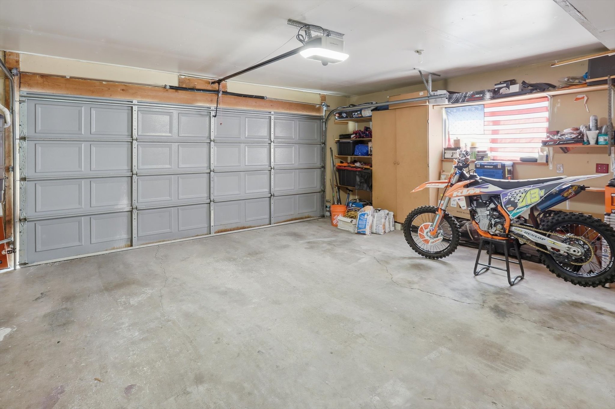 Attached garage featuring a light gray sectional door, automatic opener, concrete flooring, and built-in shelving