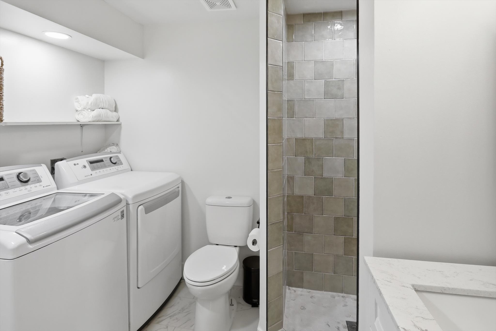 Full bathroom featuring a walk-in shower with square tiled surround, white toilet, and a vanity with a white countertop and integrated sink