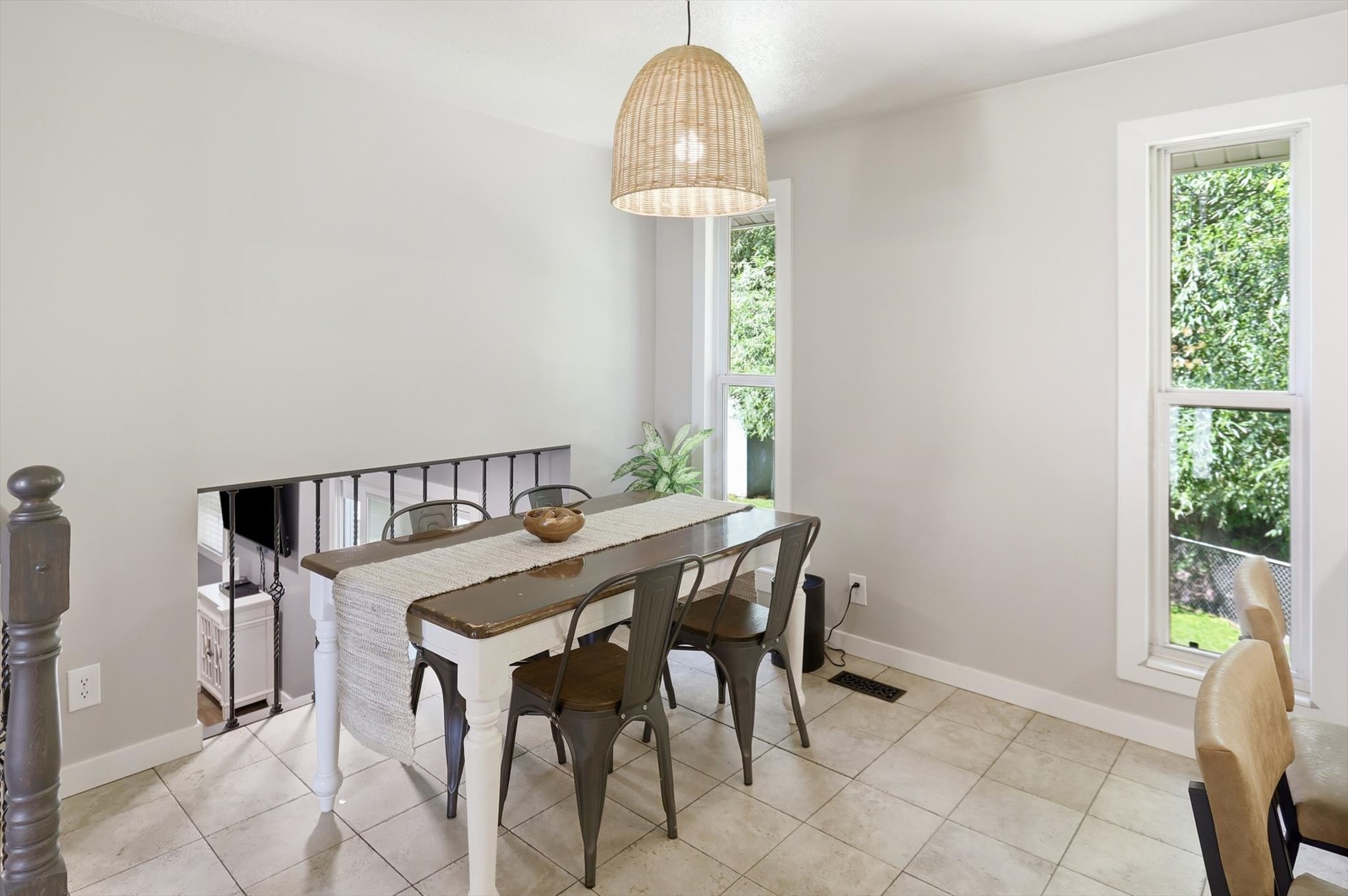 Dining area featuring light tile flooring, two tall windows, and a woven pendant light fixture